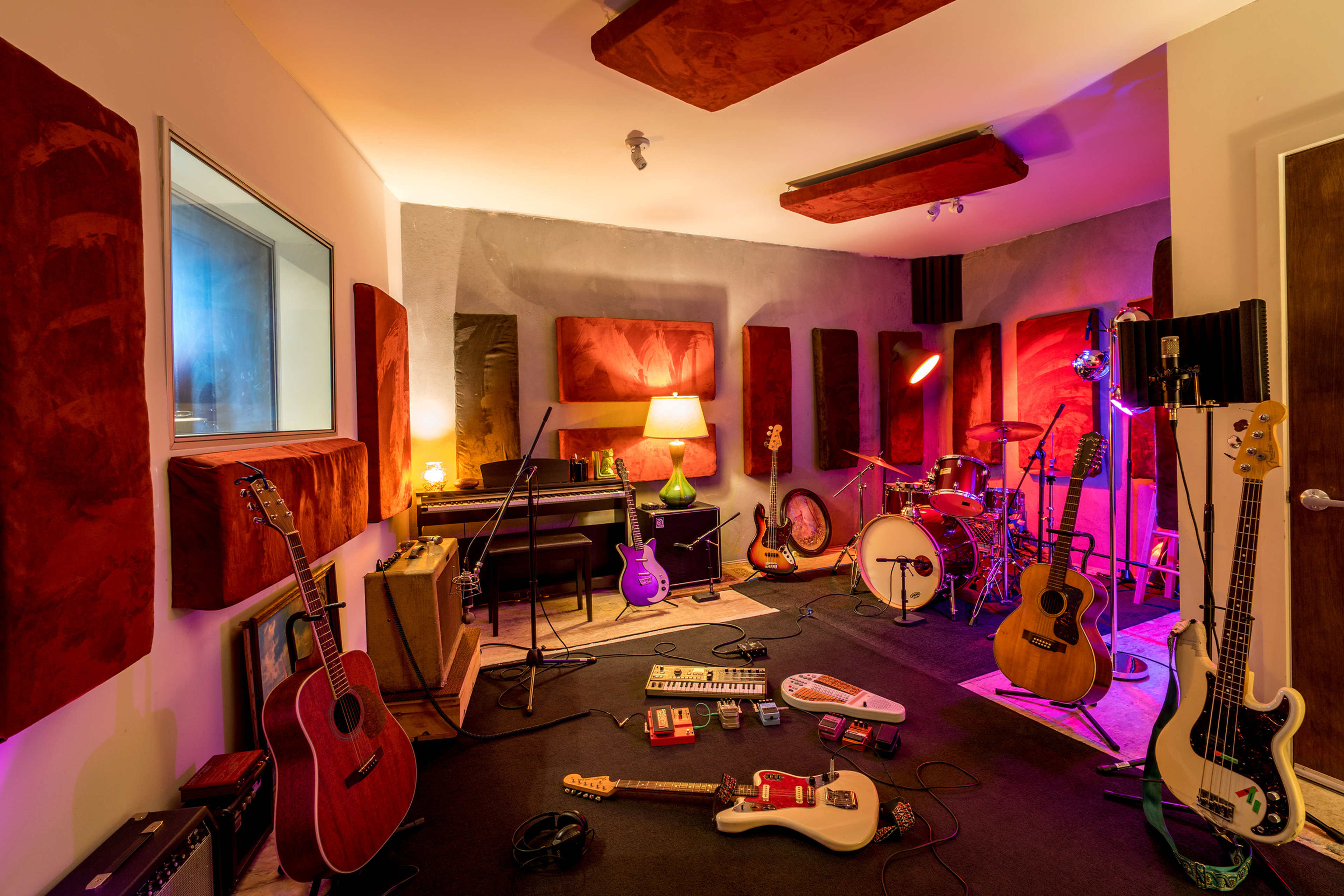 A music studio is filled with various instruments, including guitars, a drum set, and a keyboard, surrounded by soundproofing panels and ambient lighting.