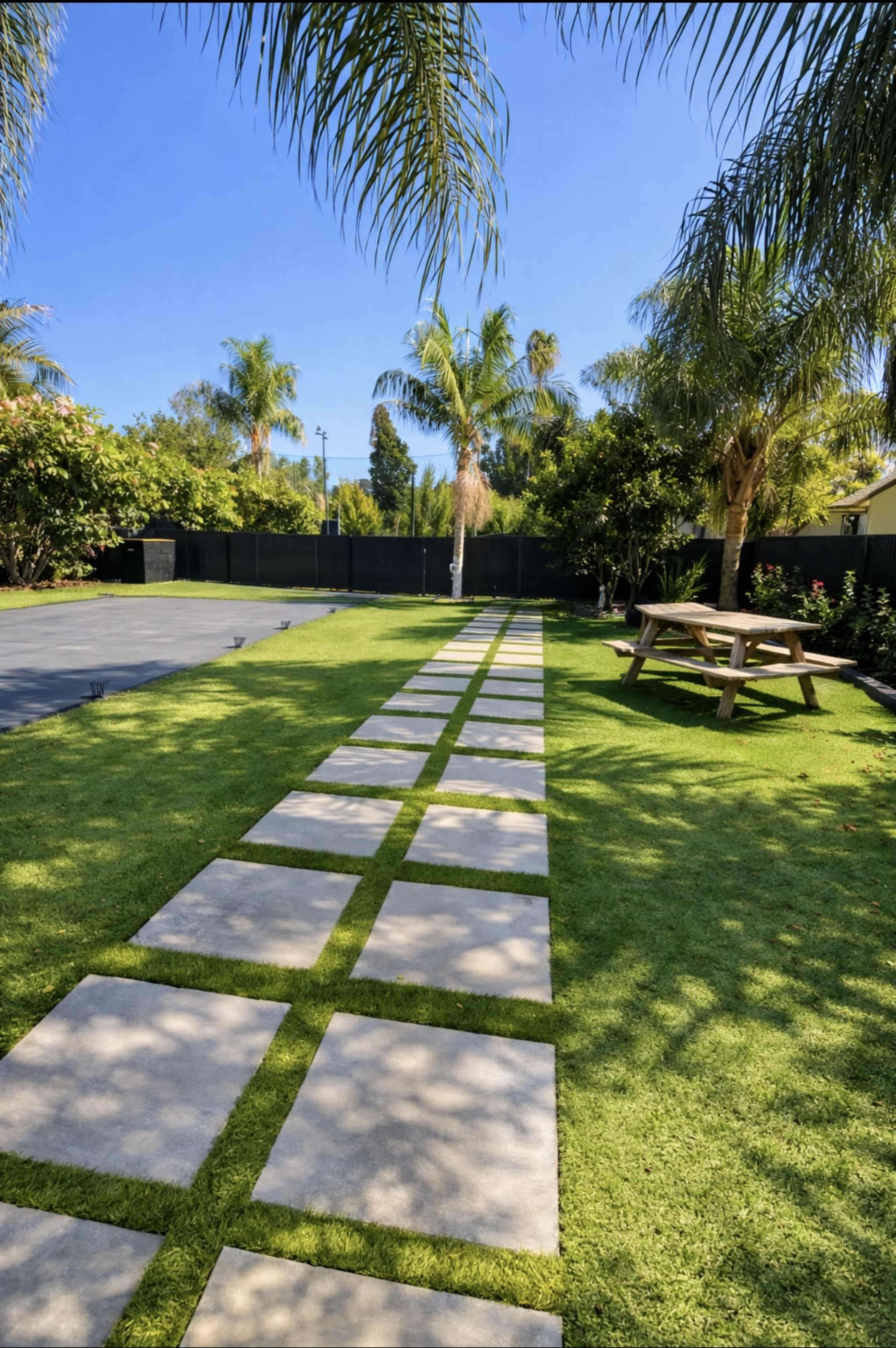 A pathway of stone slabs leads through a vibrant green lawn bordered by palm trees and shrubbery.