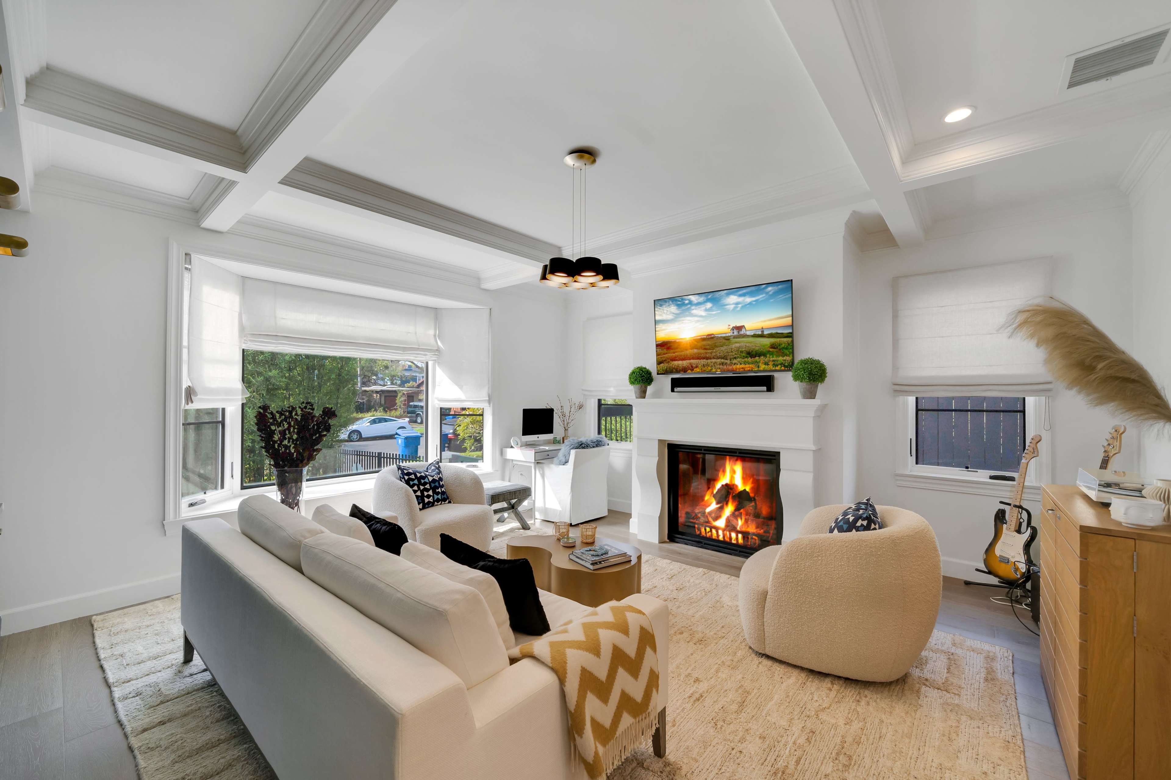 A bright living room features a fireplace, a large television mounted on the wall, and modern furniture arranged around a rug.
