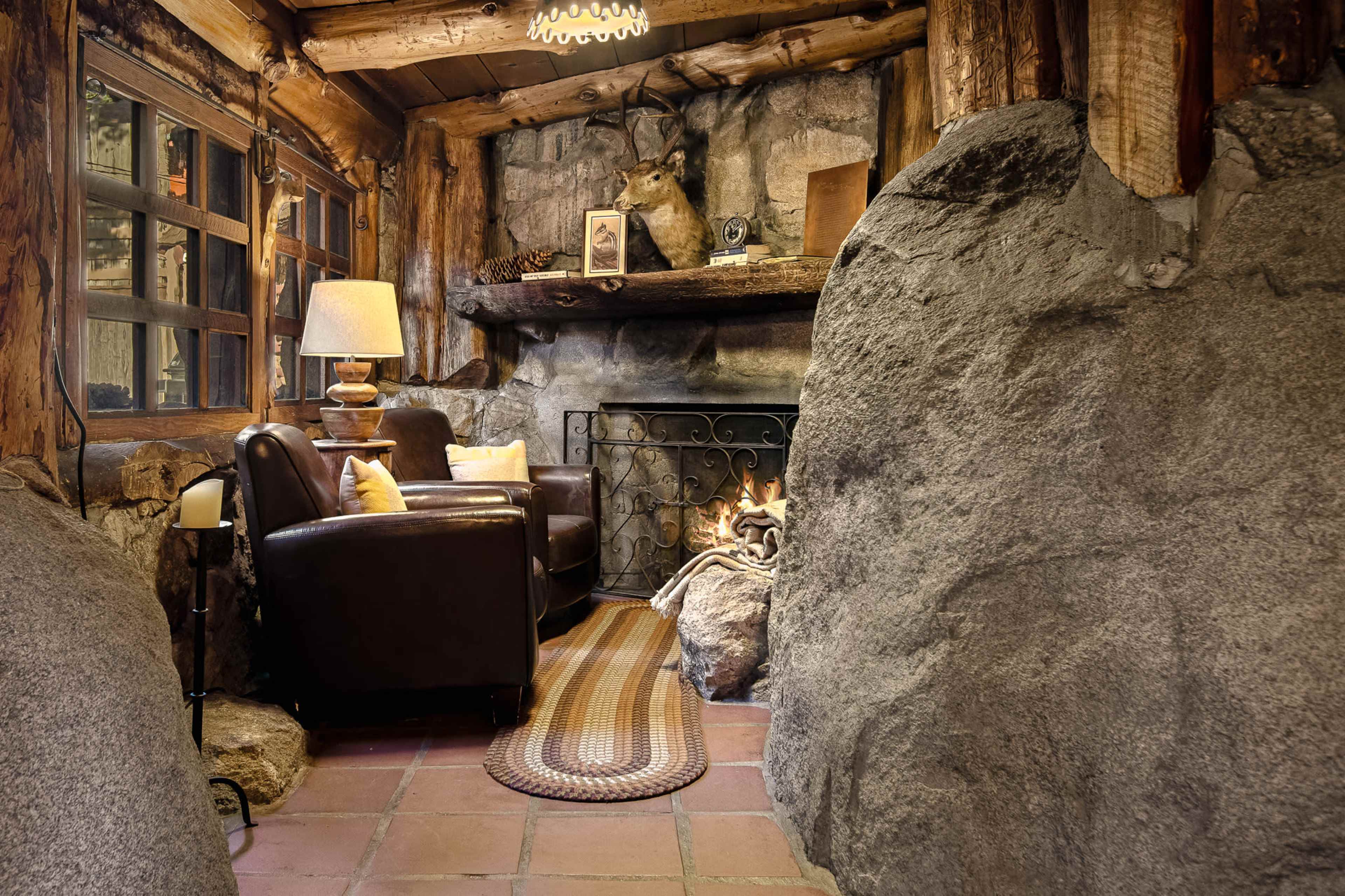 The image shows a rustic living room with stone walls, a fireplace, and two brown armchairs.