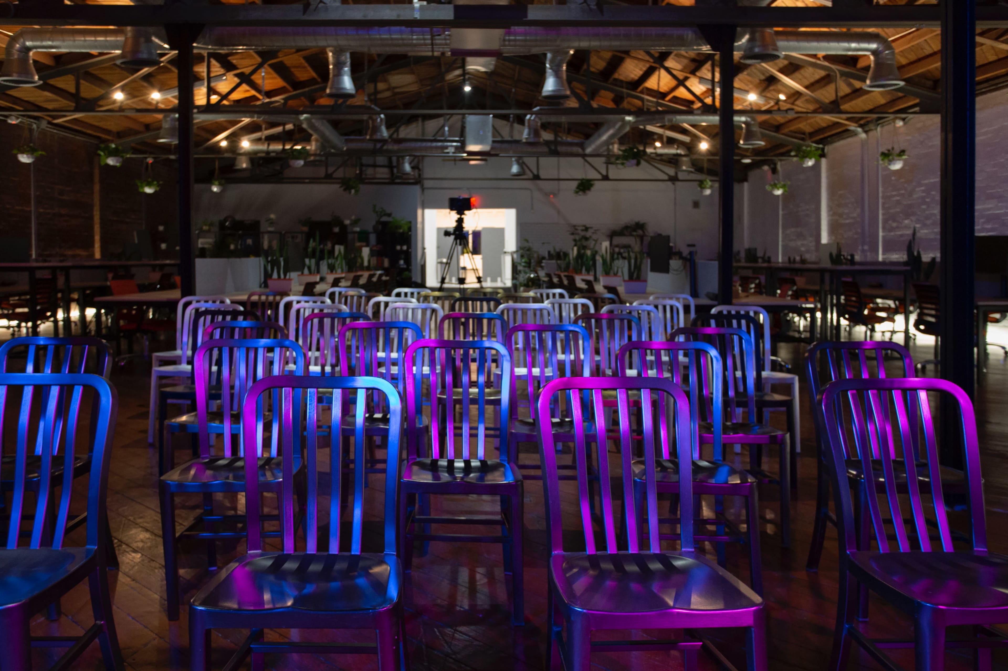 A row of metal chairs arranged in a large, well-lit venue with a wooden floor and industrial-style decor.