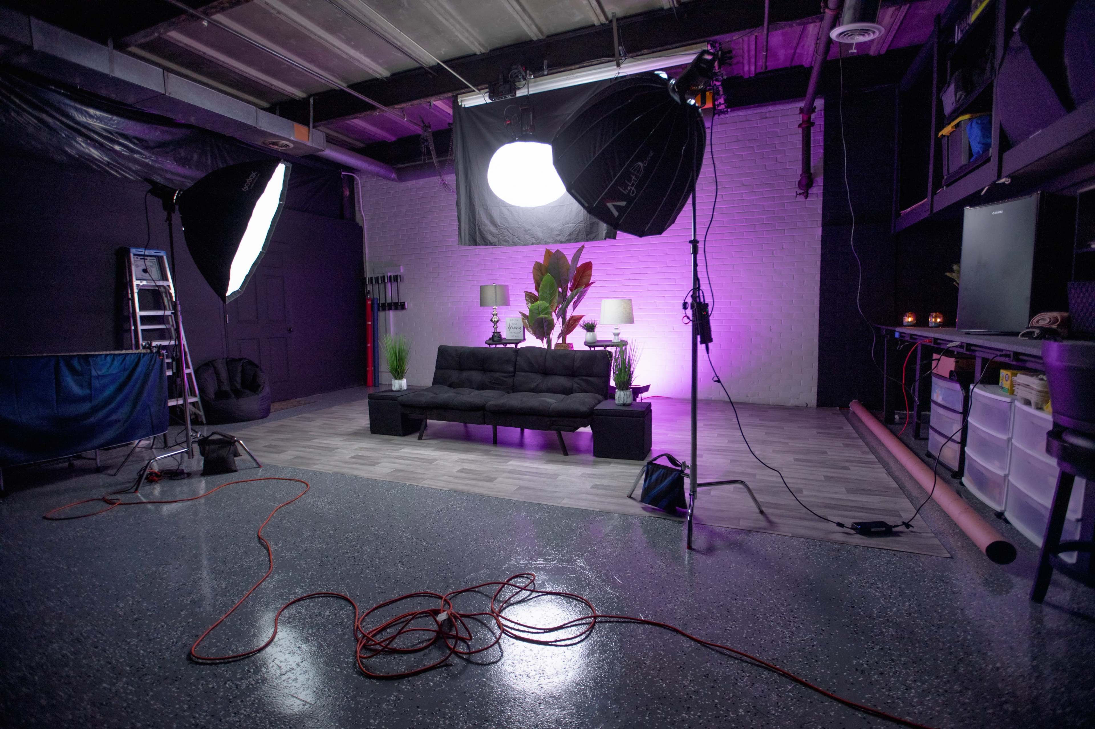 A photography studio with a black sofa, lighting equipment, and a plant, set against a backdrop of purple lighting.