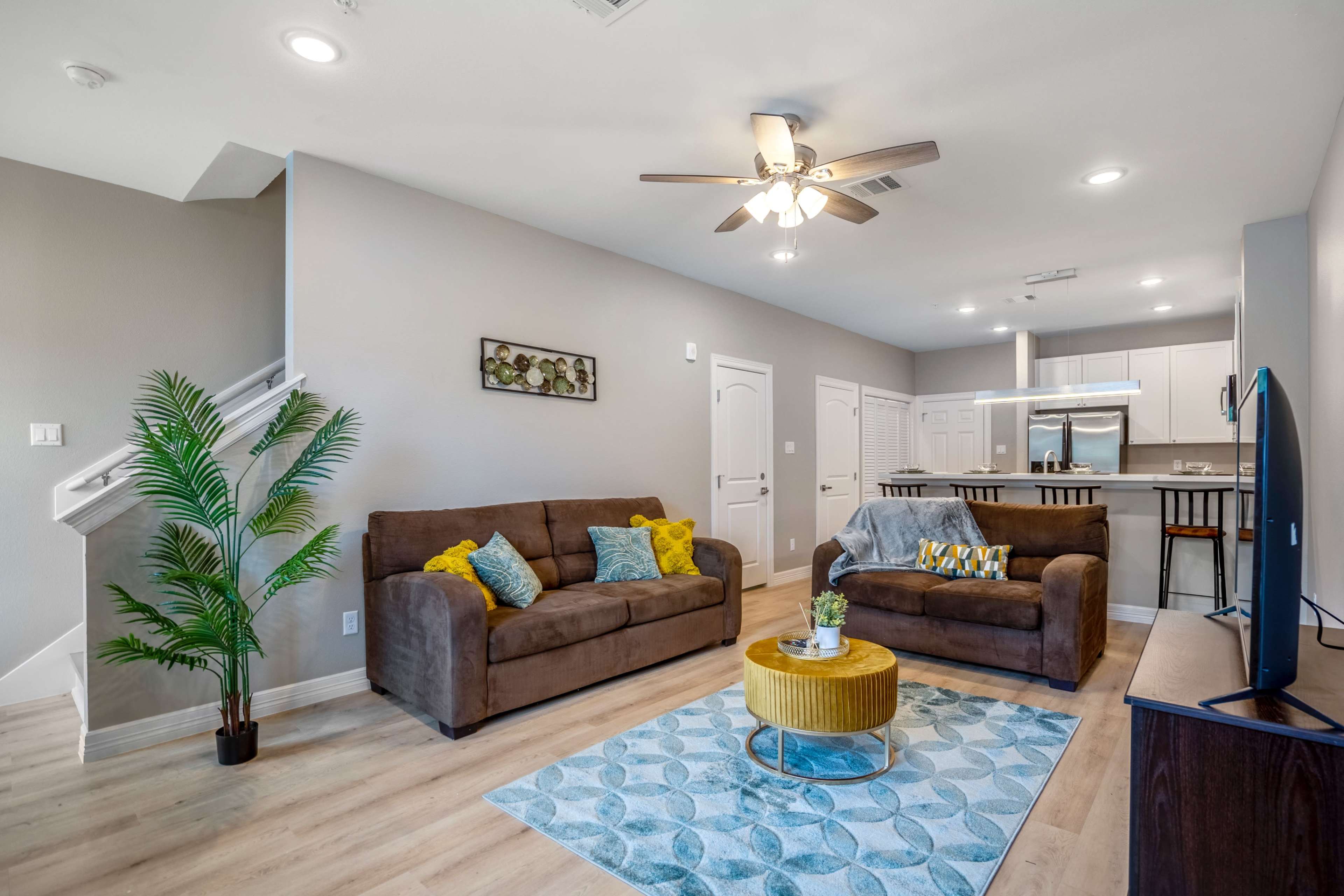 A modern living room with two brown sofas, a yellow coffee table, and a staircase leading to an upper level.