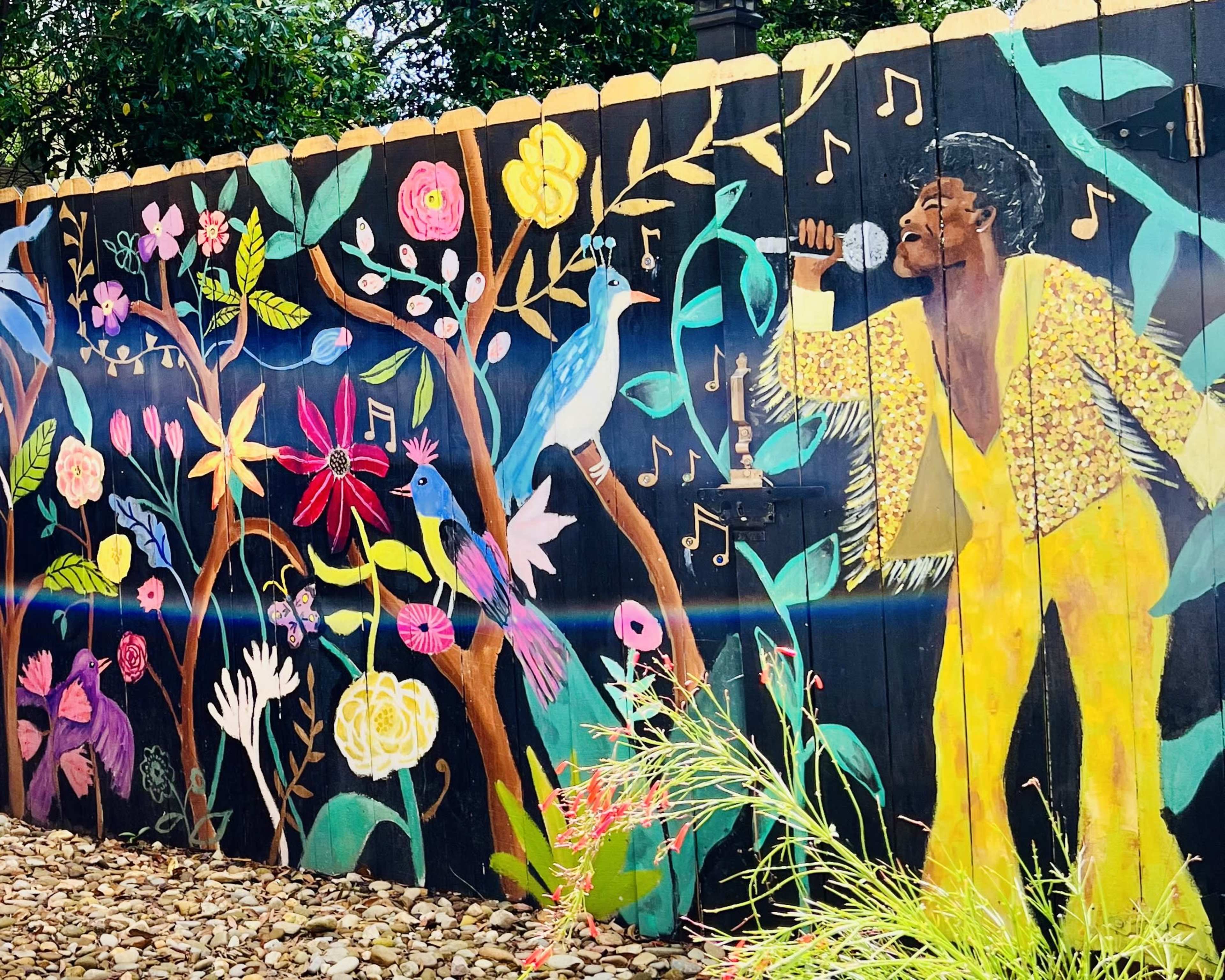 A vibrant mural on a wooden fence, depicting a singer in a sparkling outfit surrounded by colorful flowers and birds, with musical notes floating in the air.
