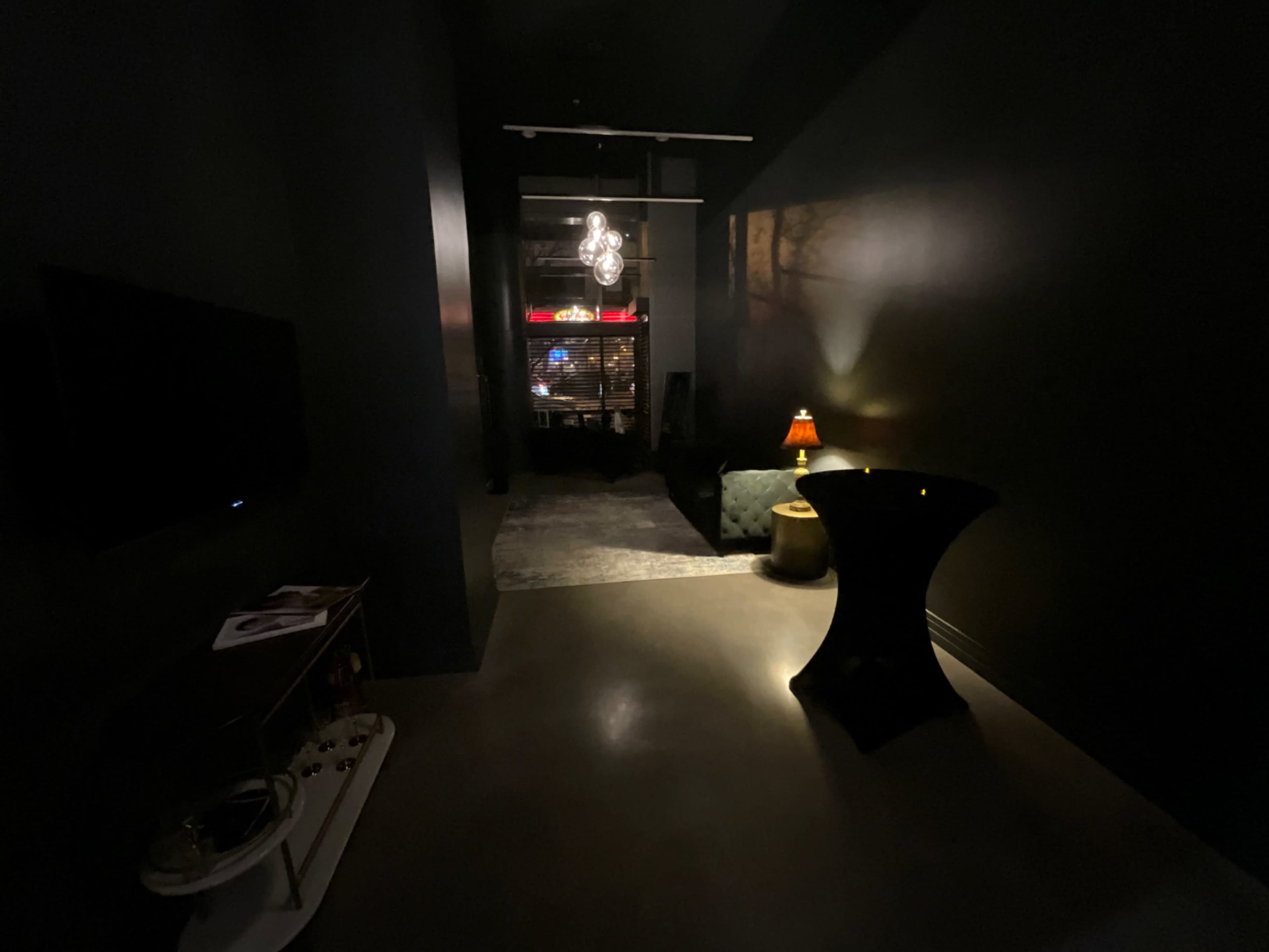 A dimly lit hallway leads to a cozy seating area, featuring a lamp and a small table.