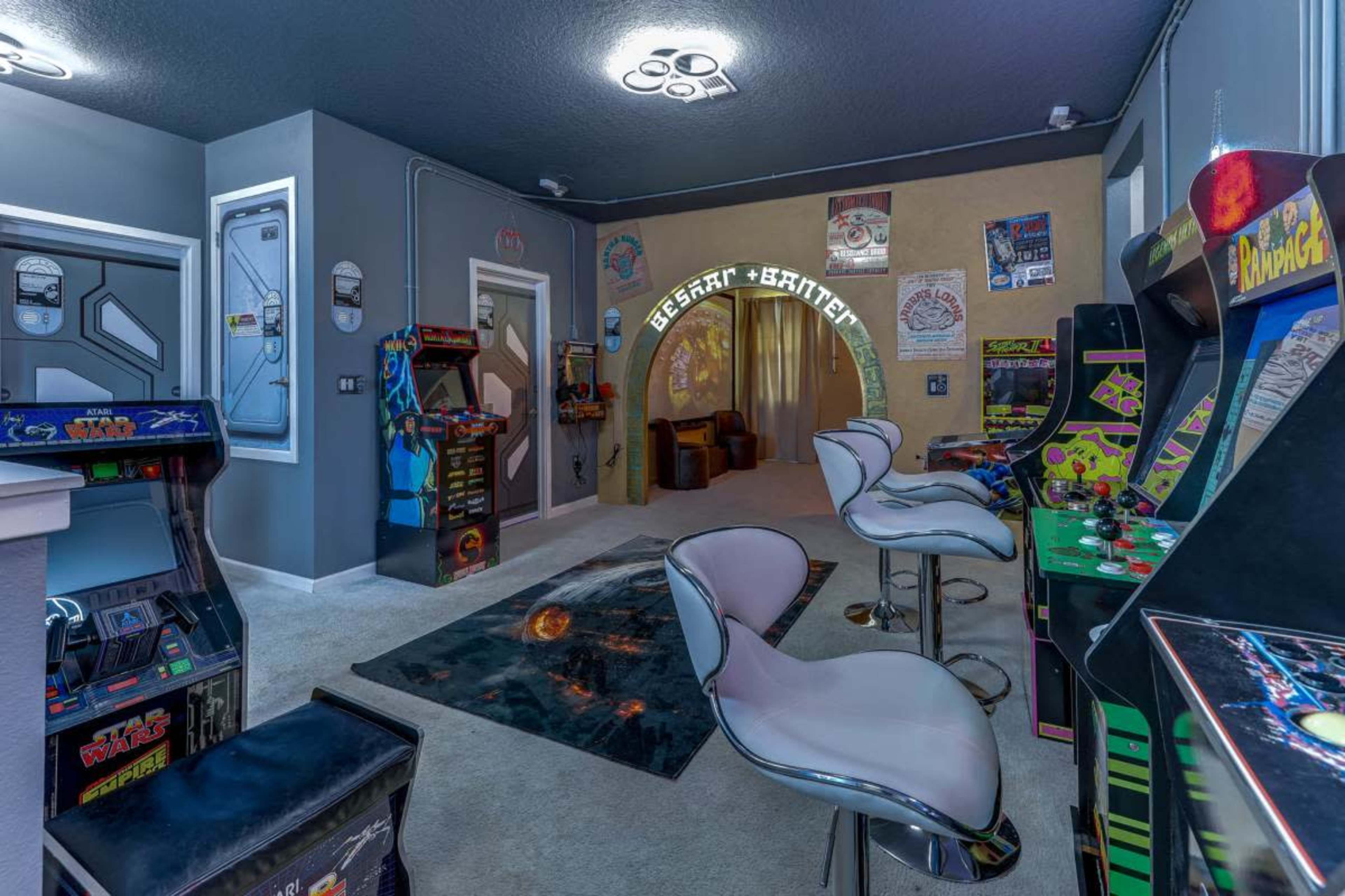 The image shows a retro-style arcade room featuring several classic arcade game machines, bar stools, and themed decor.