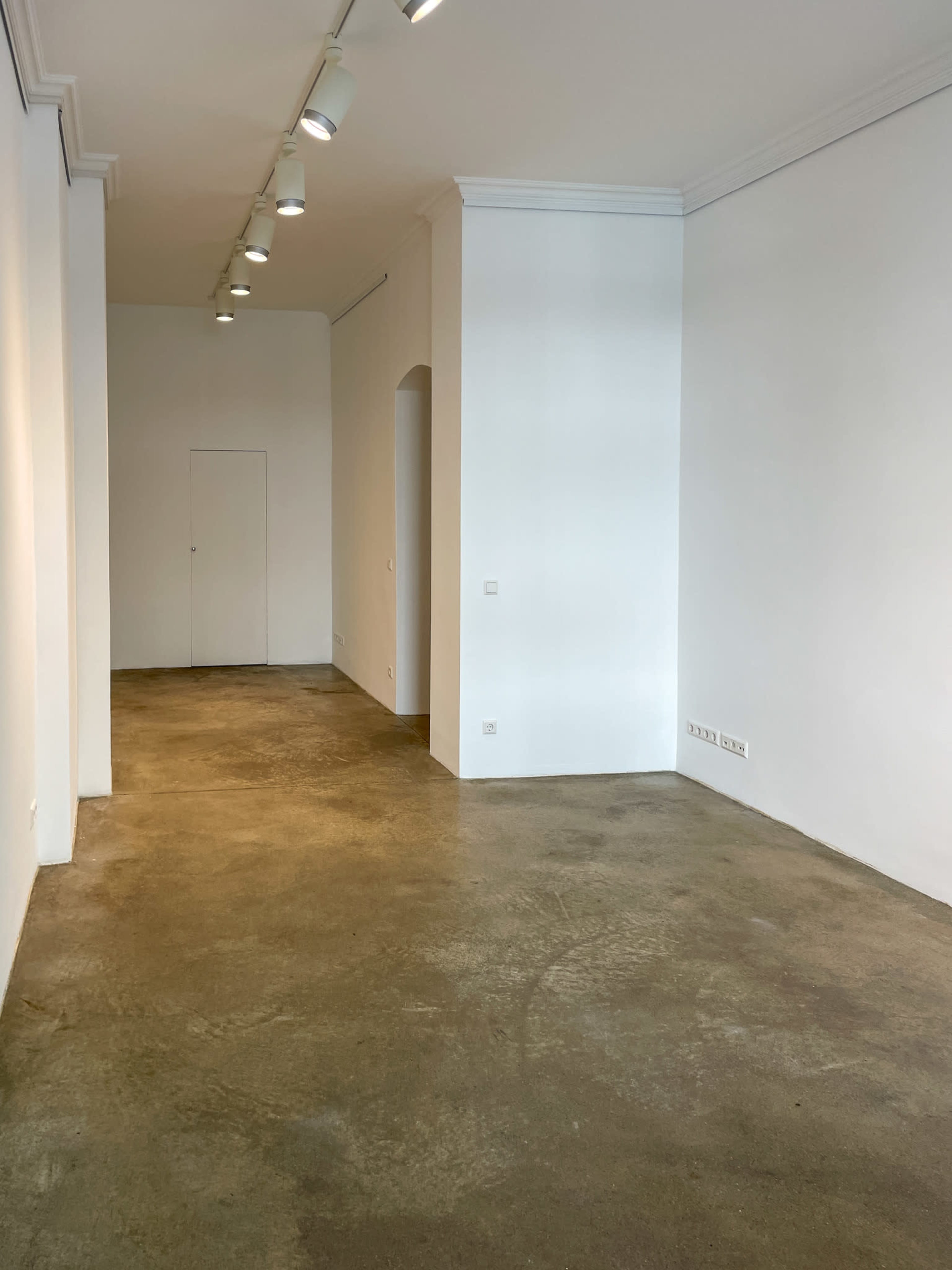 An empty room with white walls, a concrete floor, and overhead lighting.
