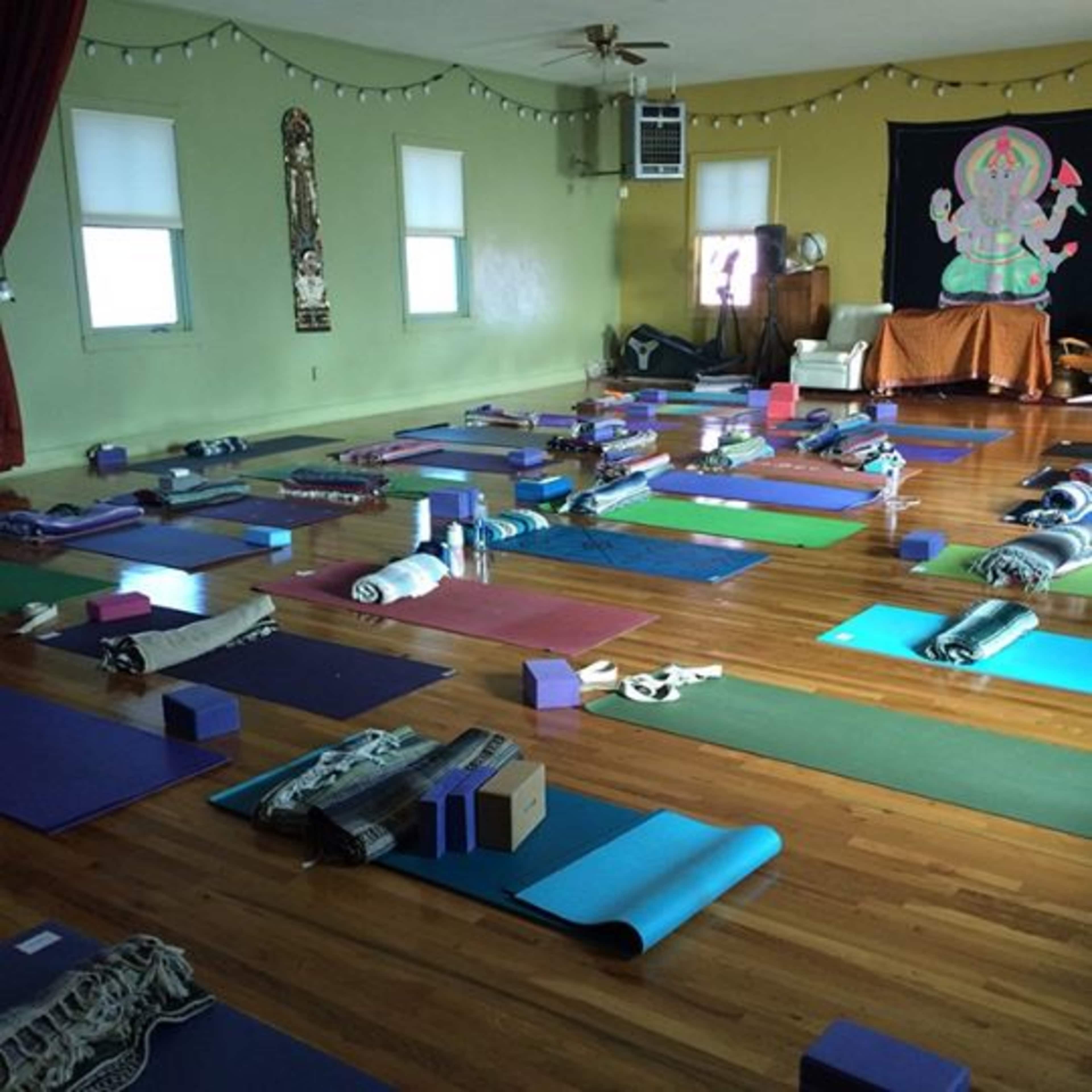 A yoga studio is arranged with various mats and props laid out evenly across the wooden floor.