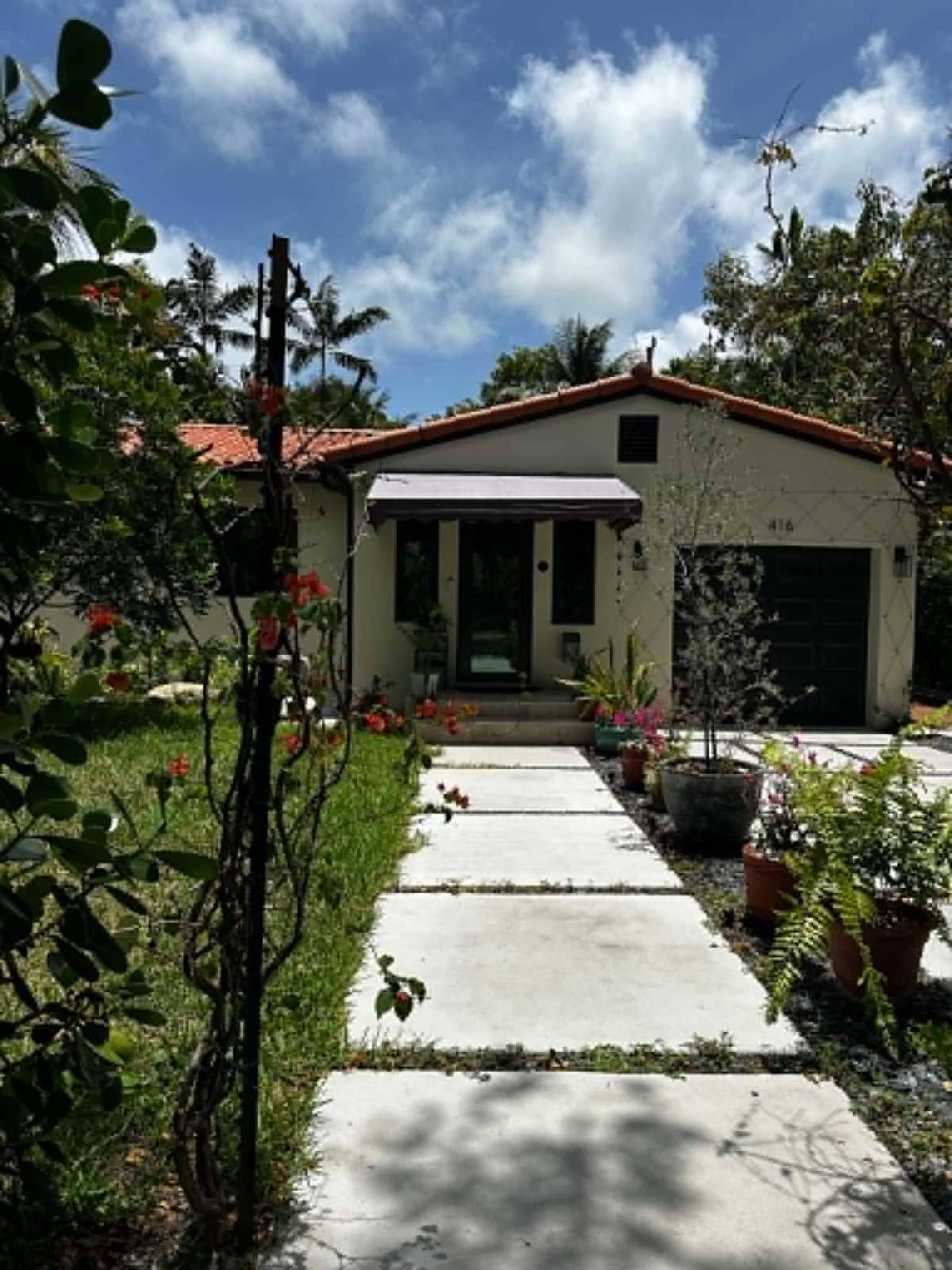 A single-story house with a red-tiled roof, surrounded by greenery and a pathway leading to the front door.