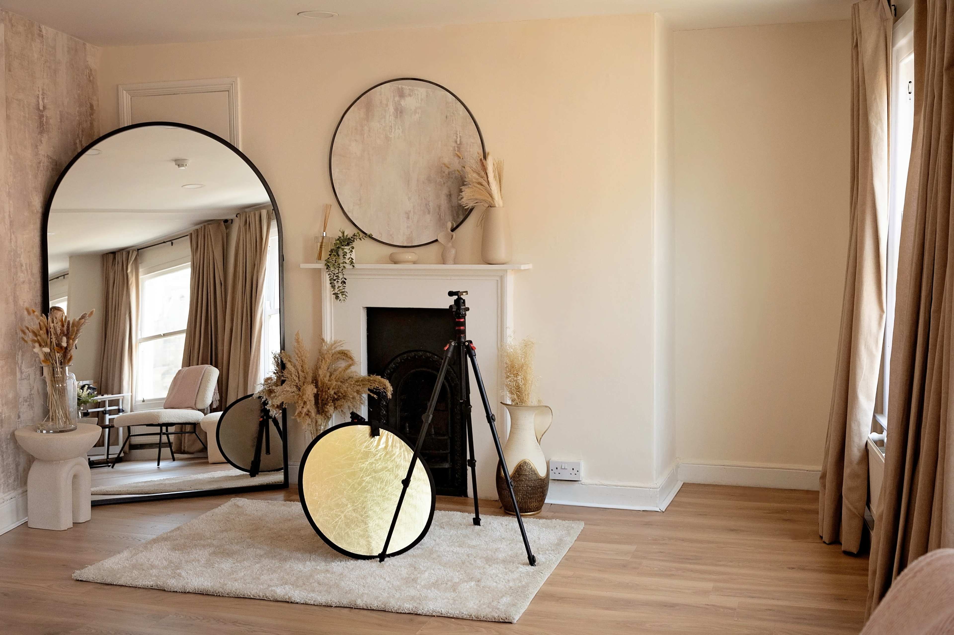 A spacious room features a large round mirror, a tripod with a reflector, and decorative elements arranged around a fireplace.