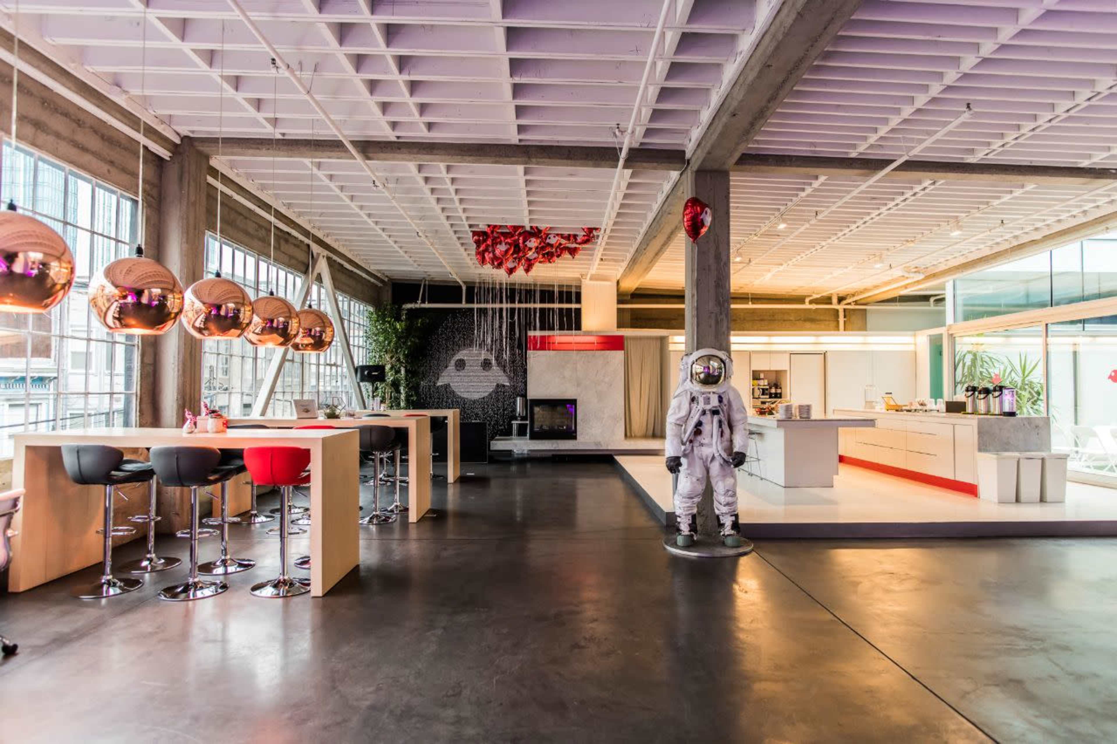 A modern, spacious interior with a kitchen, dining area featuring metallic pendant lights, and an astronaut figure standing in the foreground.