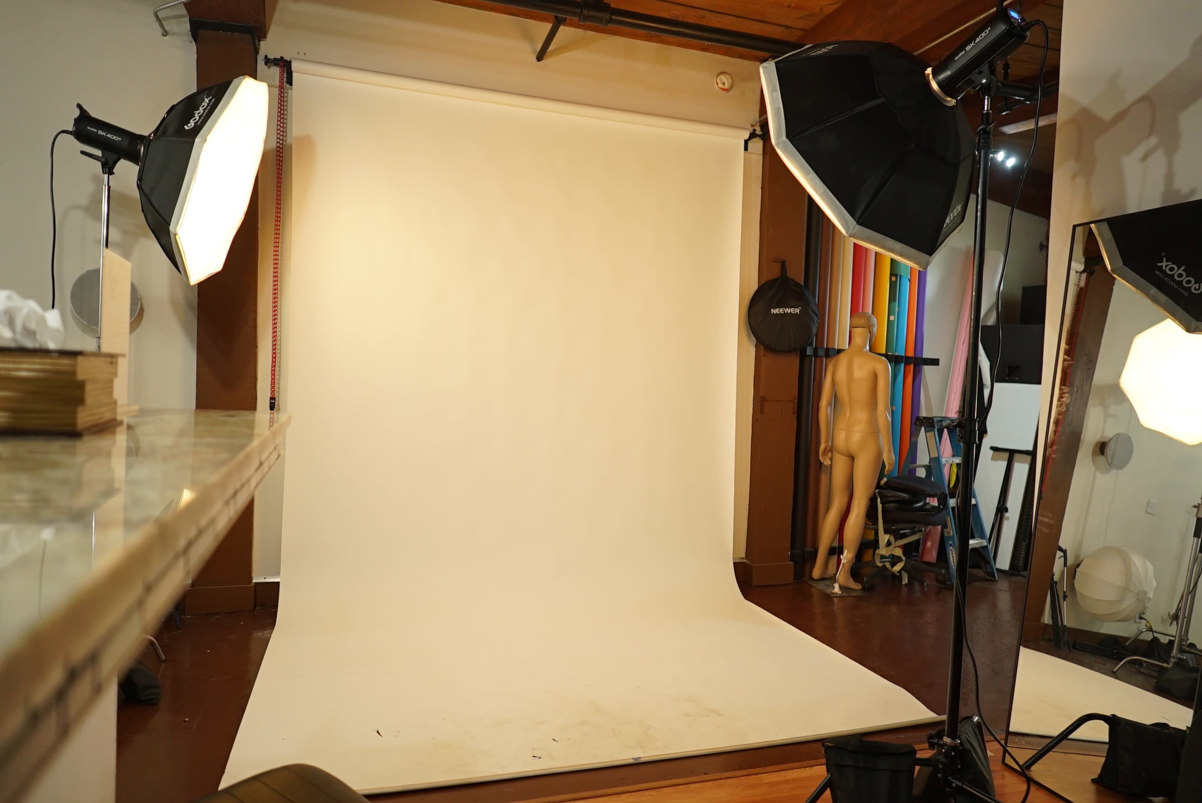 The image shows a photography studio with a plain white backdrop, positioned studio lights, and a mannequin in the corner.