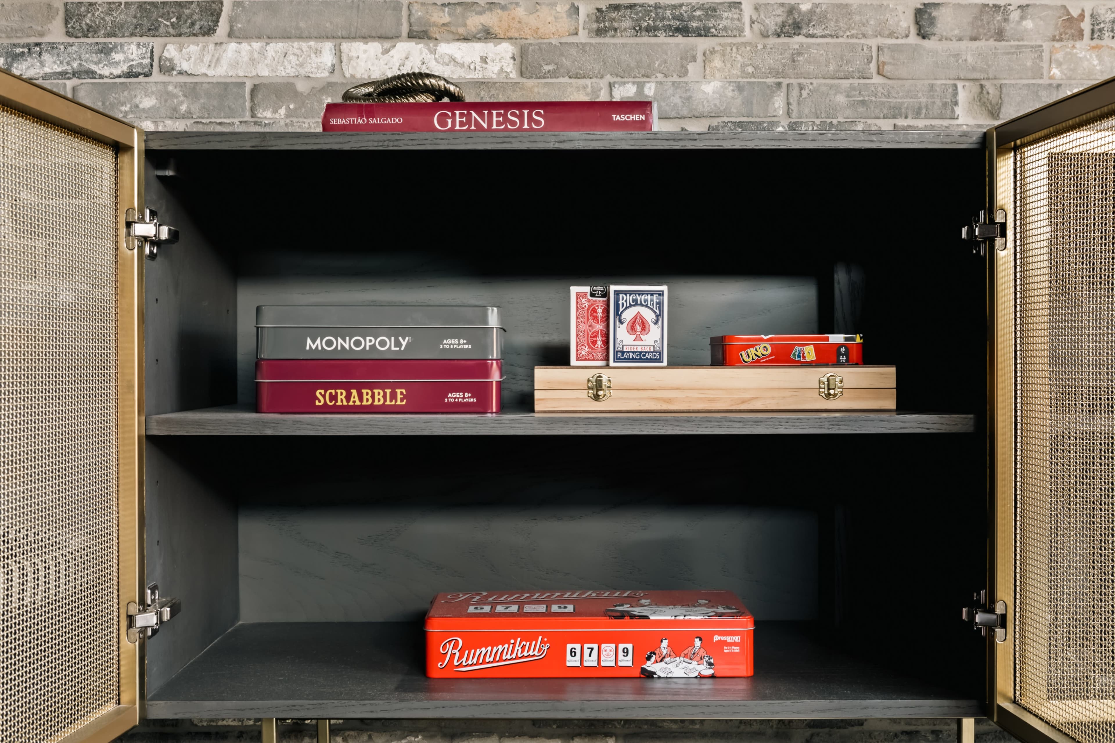 The image shows an open cabinet with various board games and a decorative box neatly arranged on its shelves.