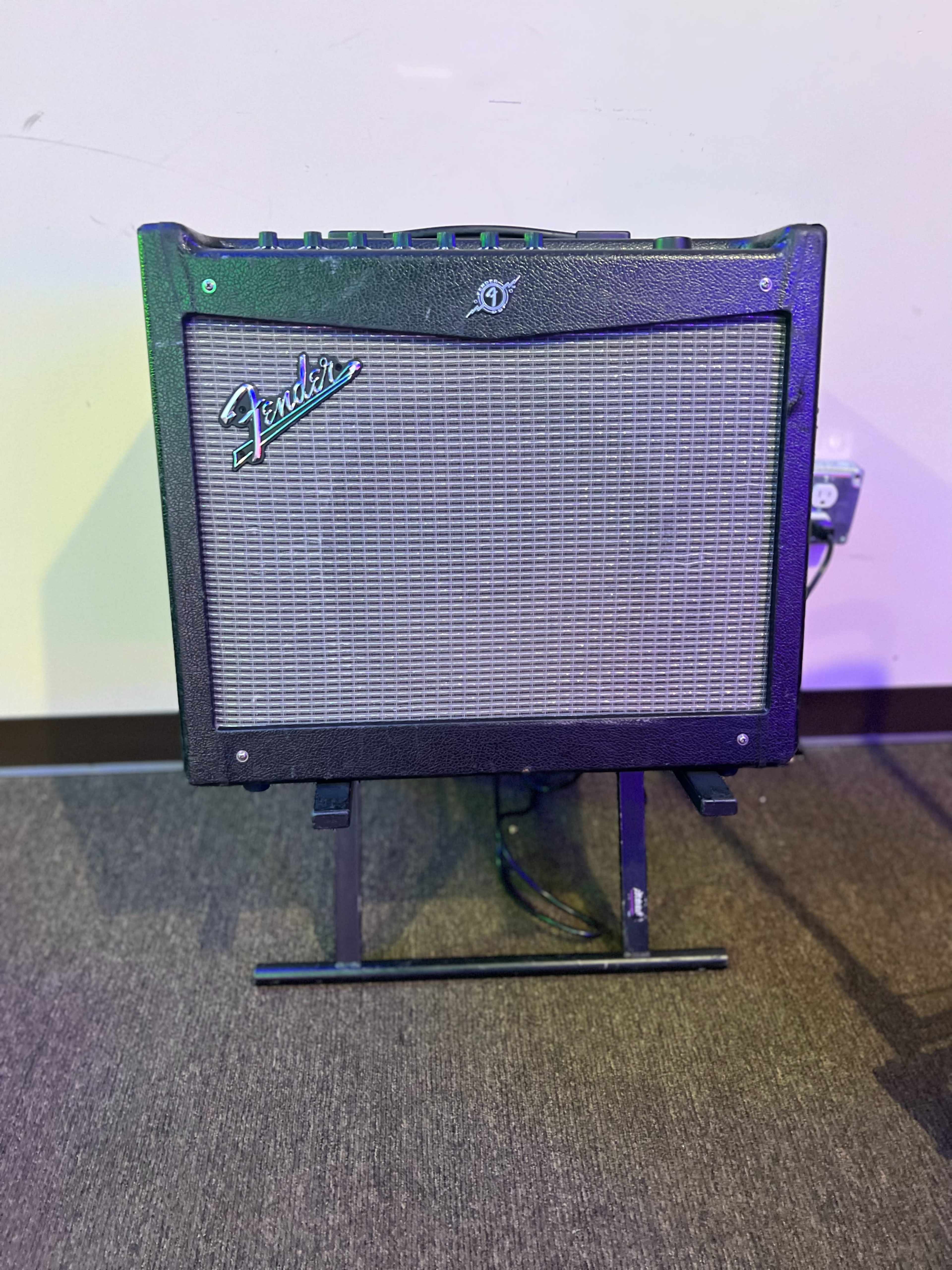 A Fender guitar amplifier is positioned on a stand against a wall.