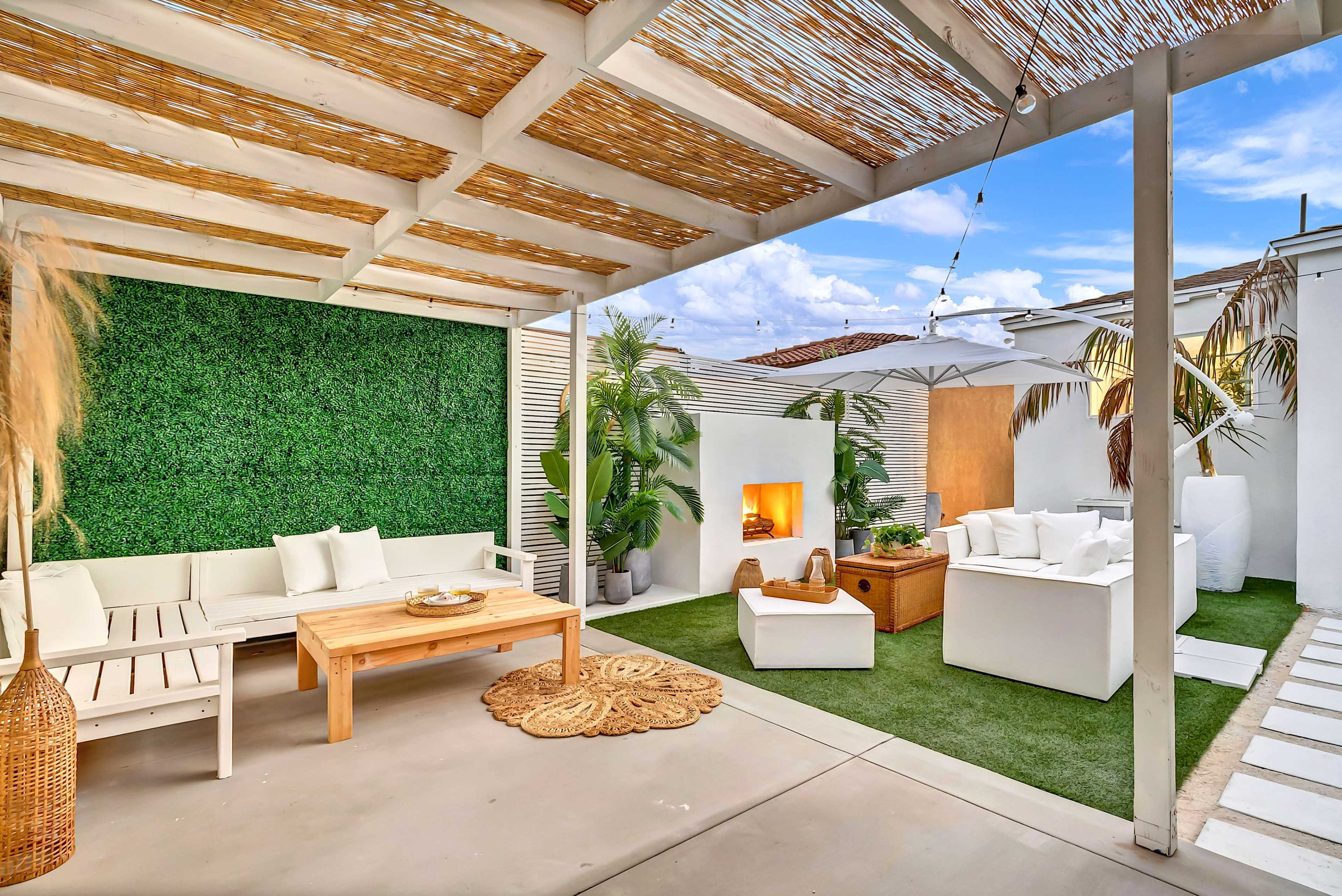A modern outdoor living space with a seating area, a fire pit, greenery, and a covered patio.
