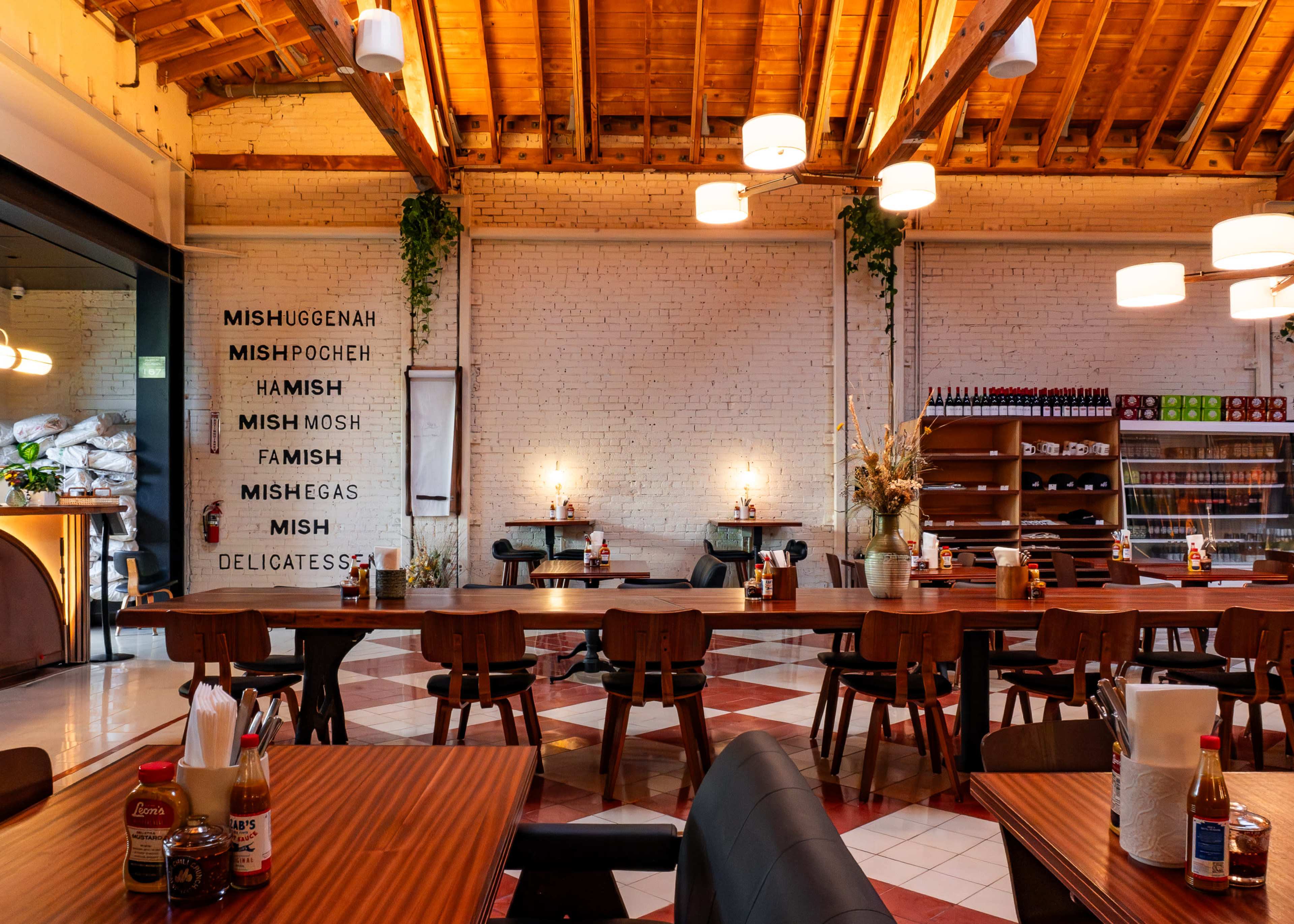 The image shows a modern restaurant interior with wooden beams, tiled flooring, and a large communal dining area featuring dark wooden tables and chairs.