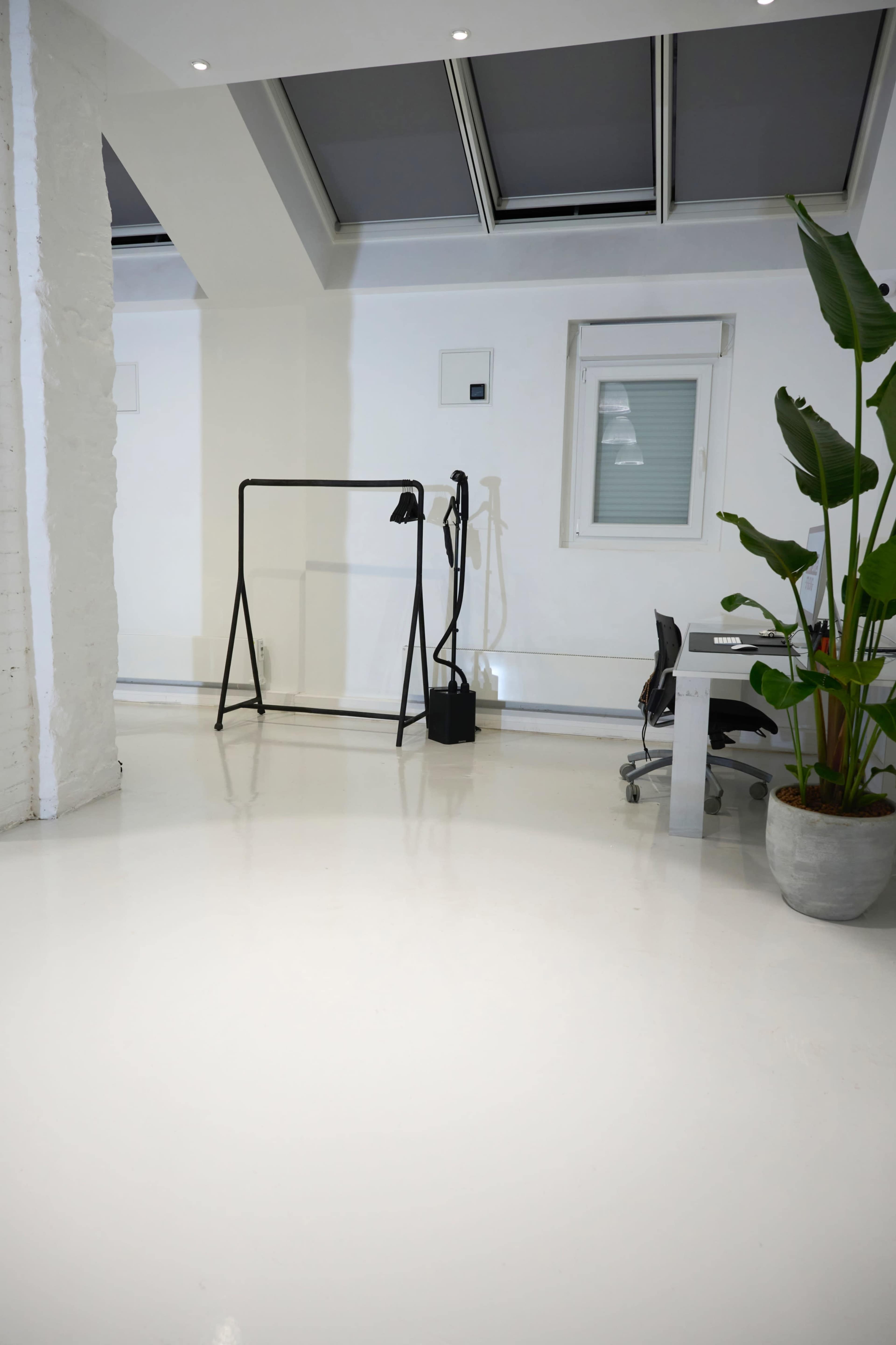 A bright, minimalistic room with a clothing rack, a desk with a chair, and a potted plant in one corner.
