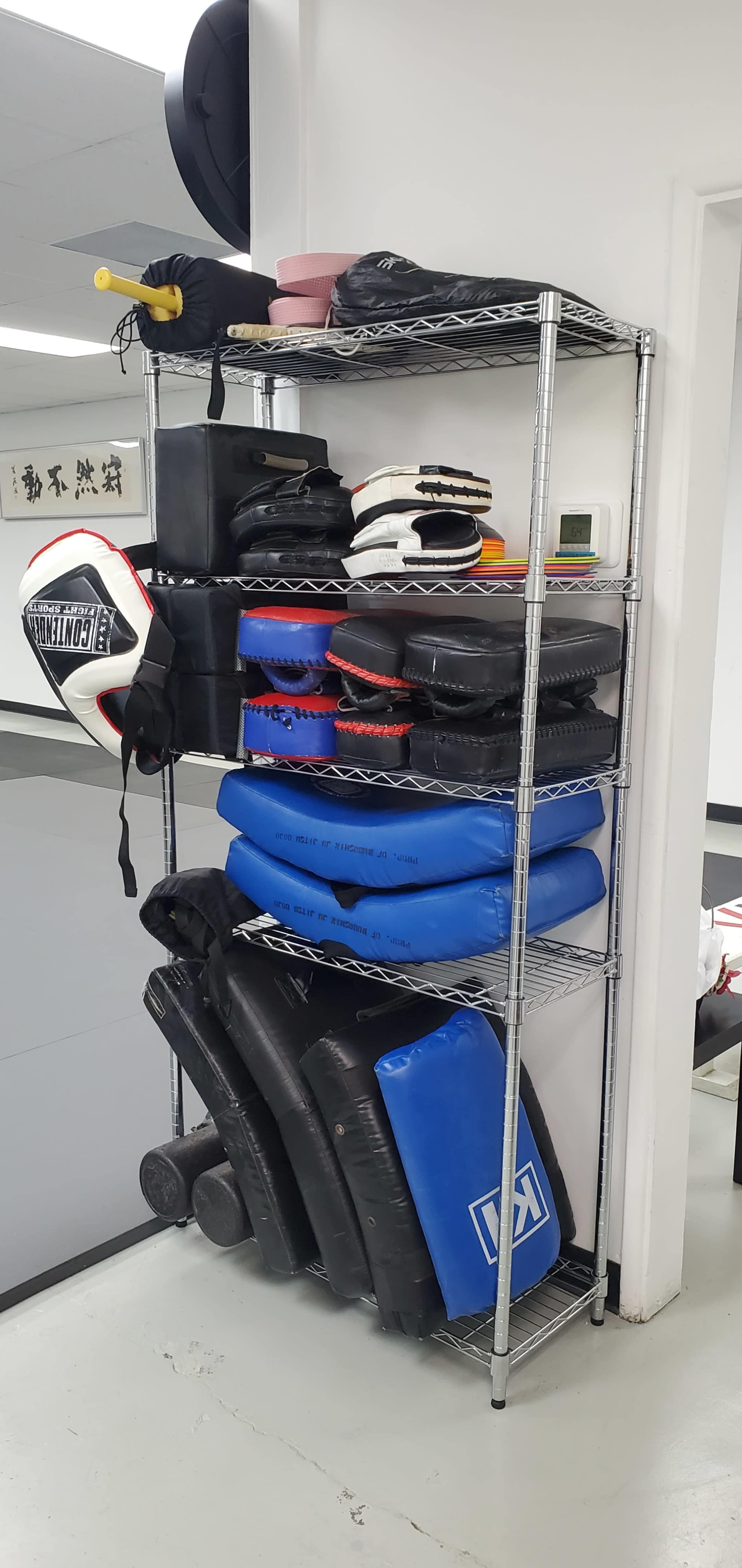 A metal shelving unit holds various pieces of boxing and martial arts equipment, including pads and protective gear.