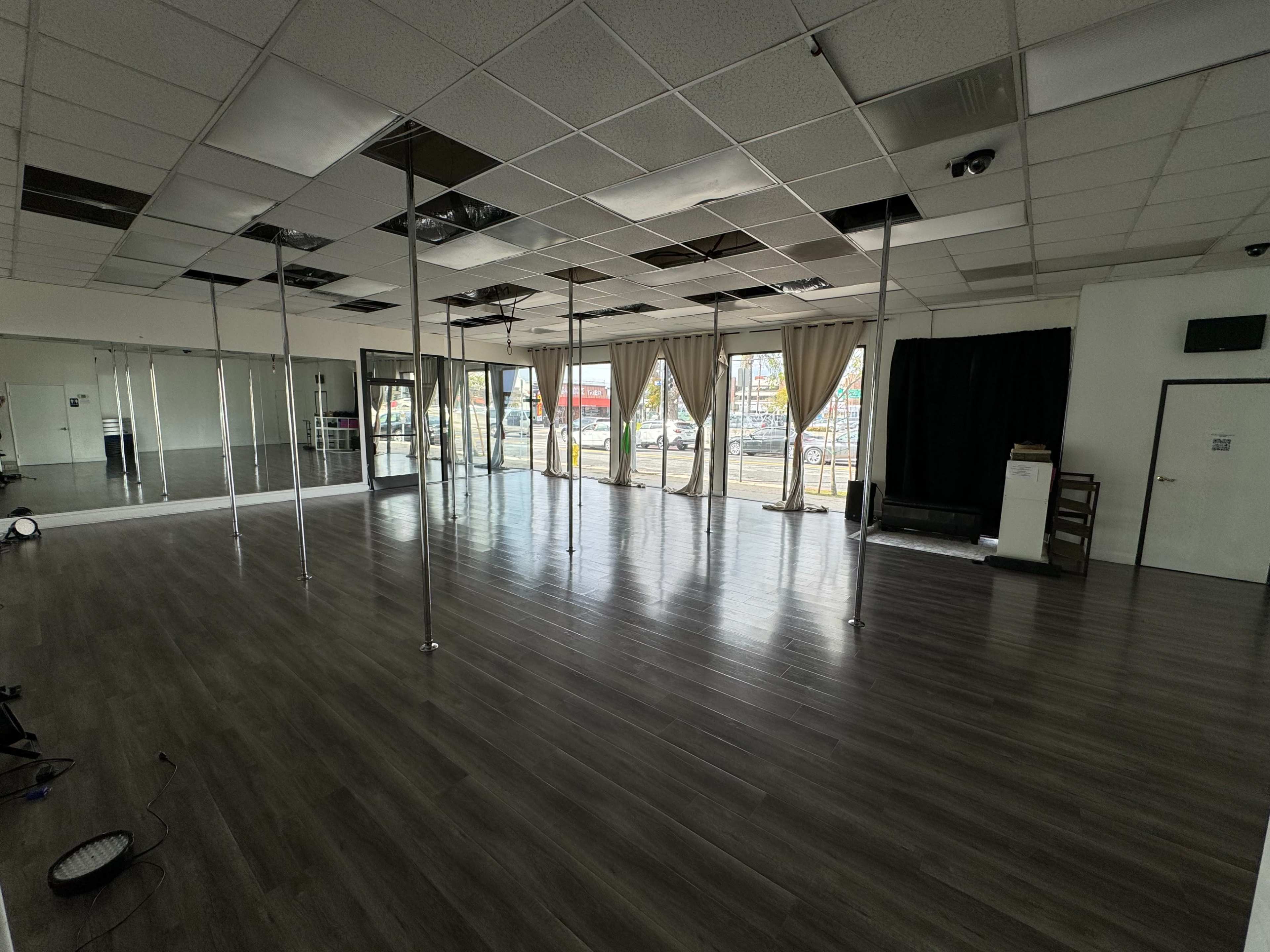 A spacious dance studio with multiple mirrored walls, poles, and large windows allowing natural light.