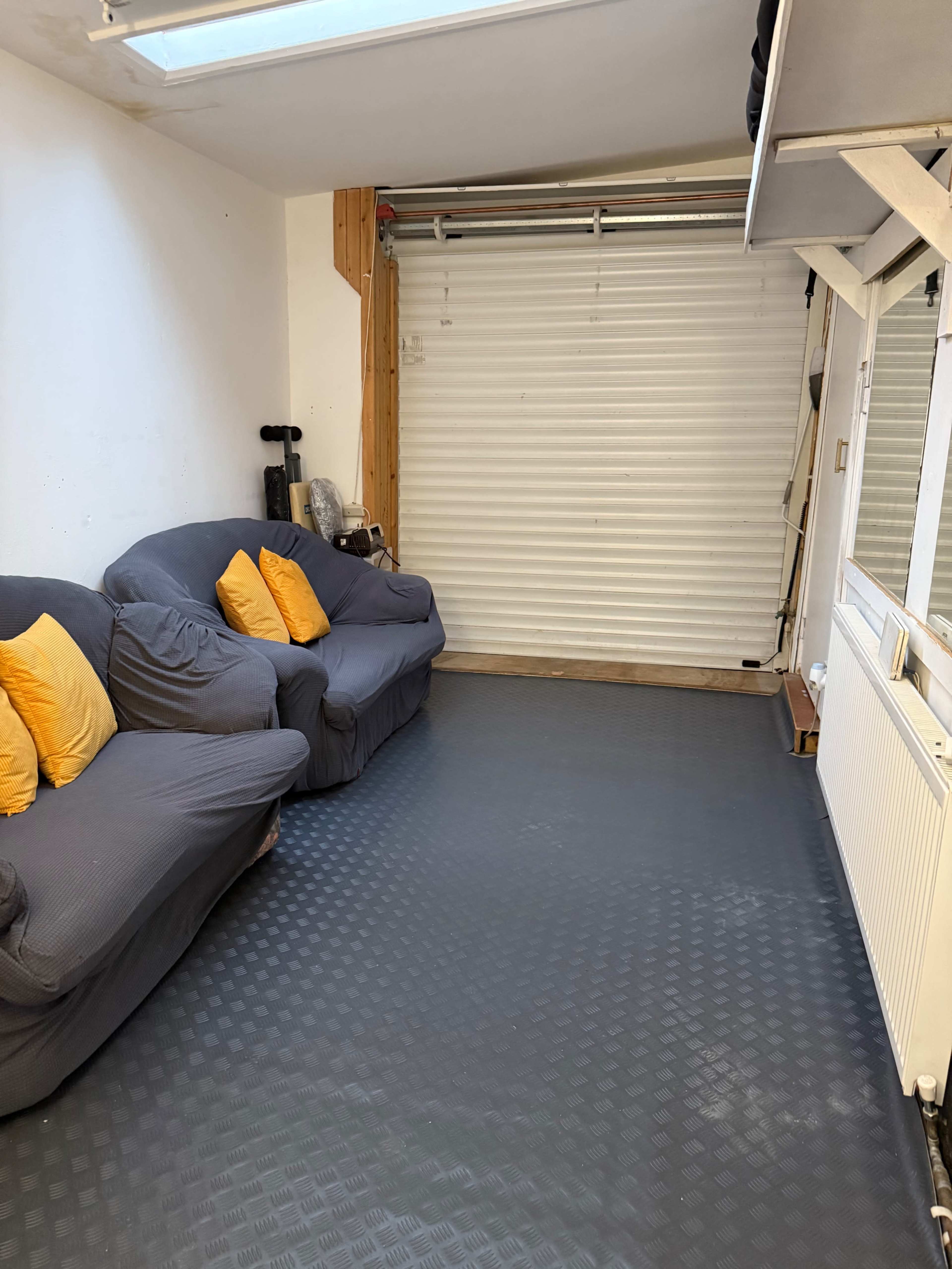 The image shows a room with two gray couches adorned with orange cushions, a slatted door at the back, and a textured black floor.