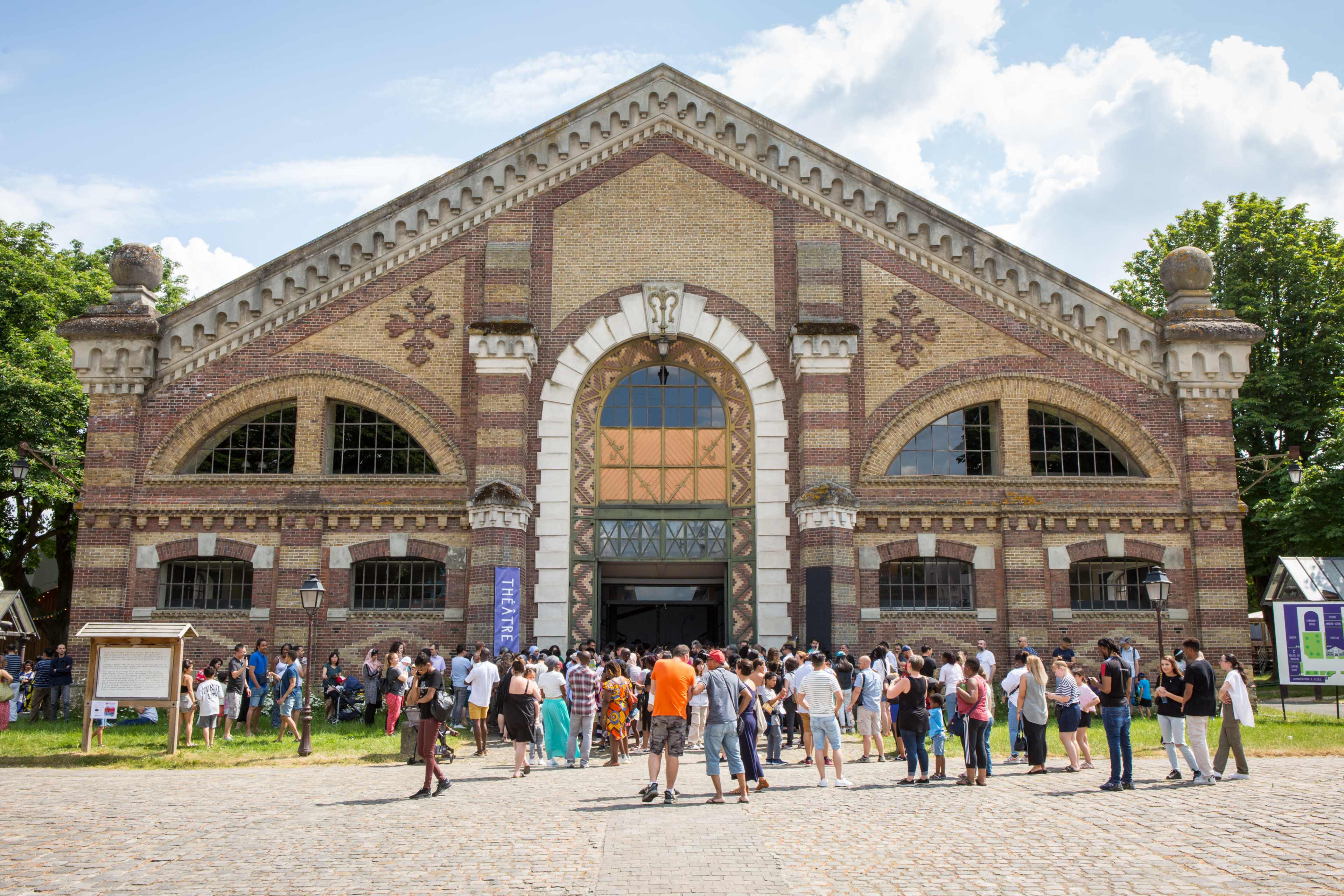 A large crowd gathers in front of a historic brick building with arched windows and an ornate entrance.