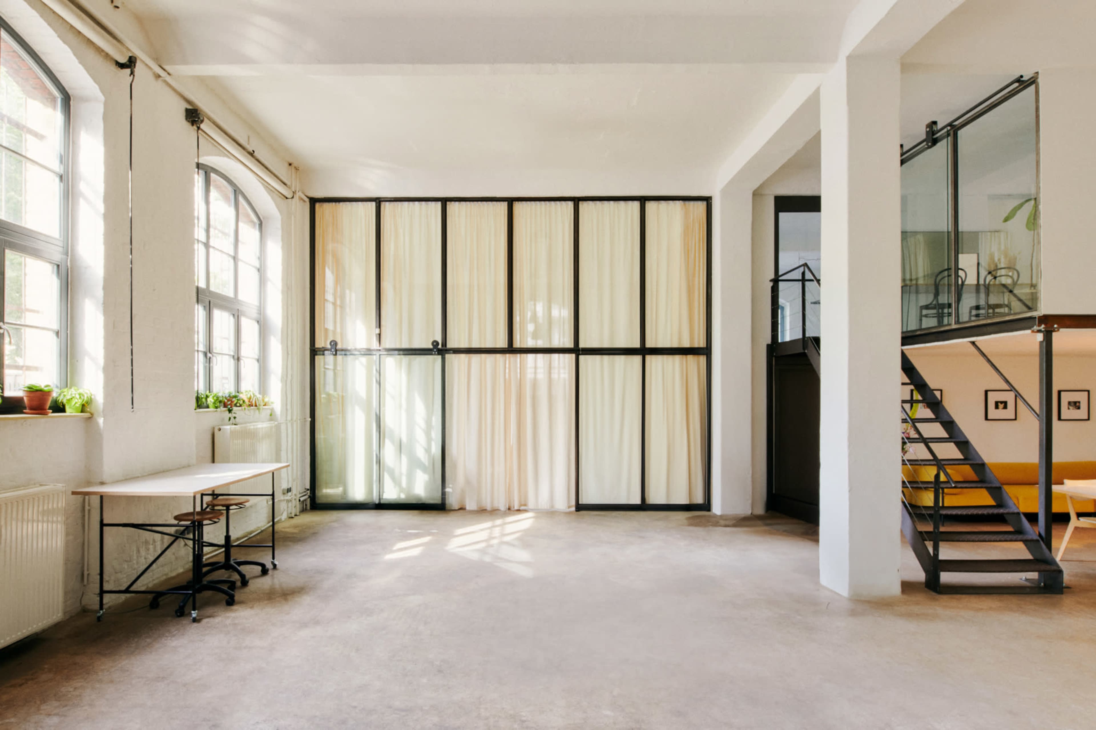 The image shows an airy, open interior space featuring large windows, a seating area, and a partition of curtains.