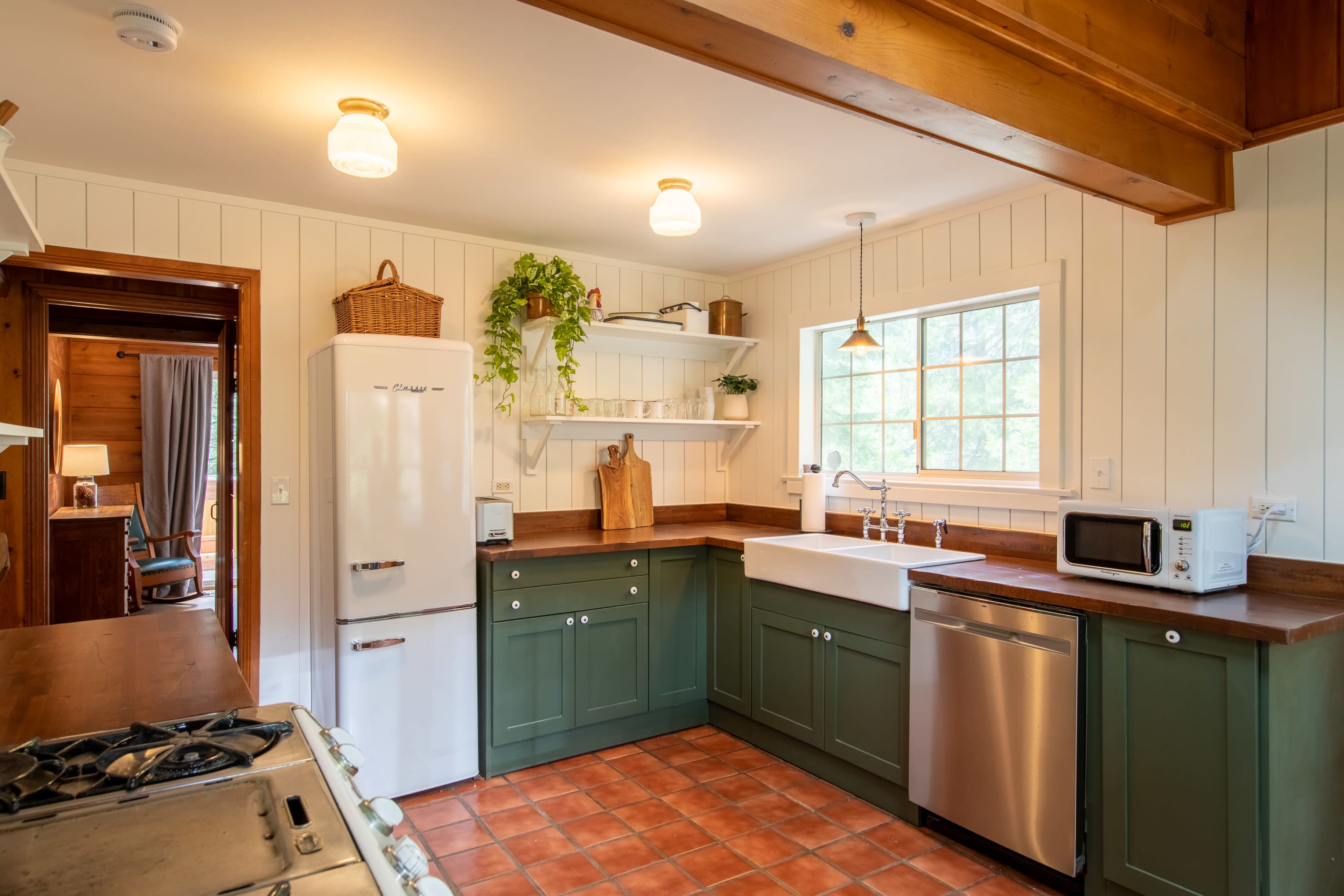 The kitchen features green cabinetry, a farmhouse sink, and wooden countertops, with a window providing natural light.