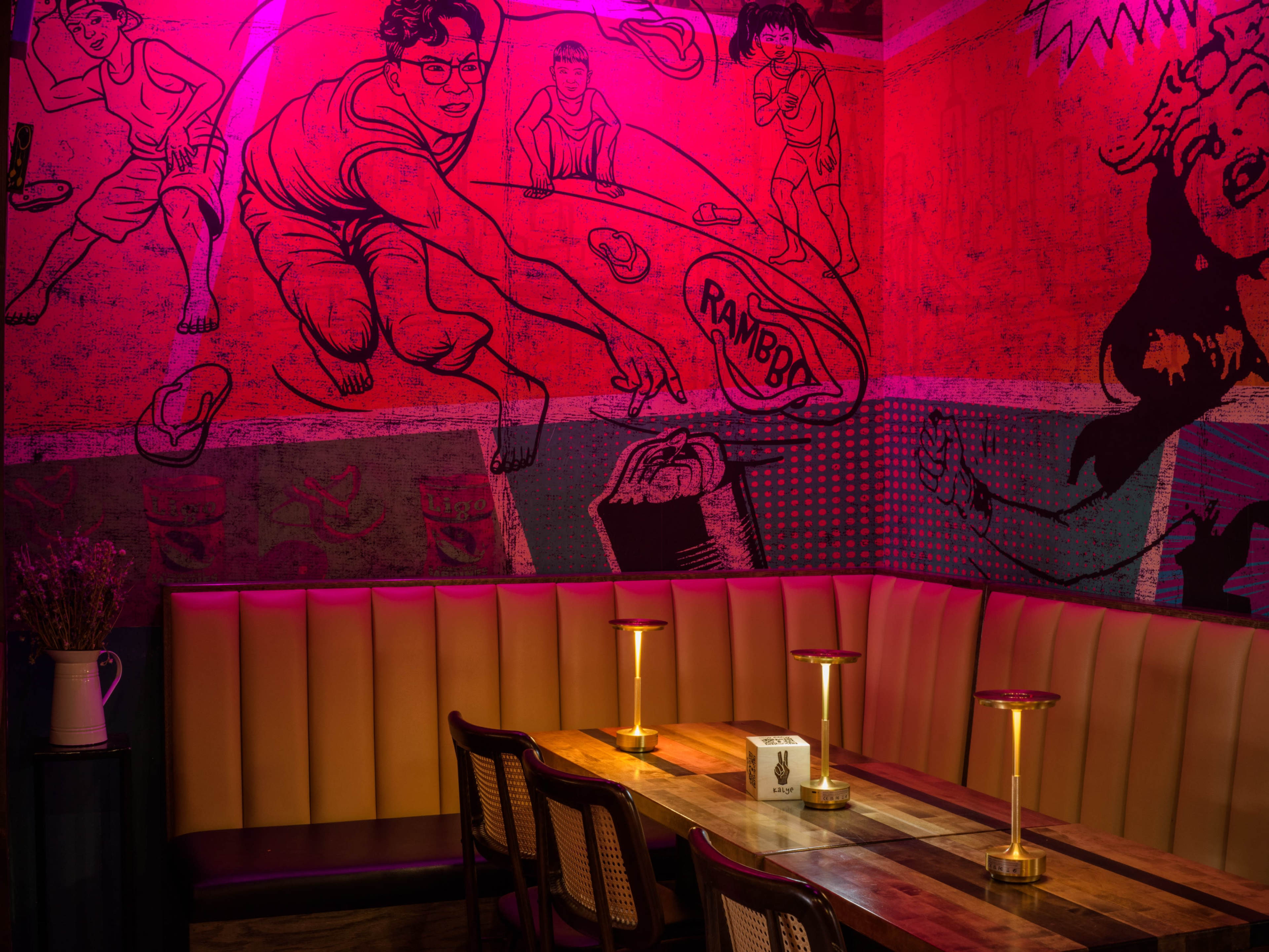The image shows a dimly lit restaurant with pink lighting and a mural depicting retro sports scenes on the wall behind a wooden table and benches.
