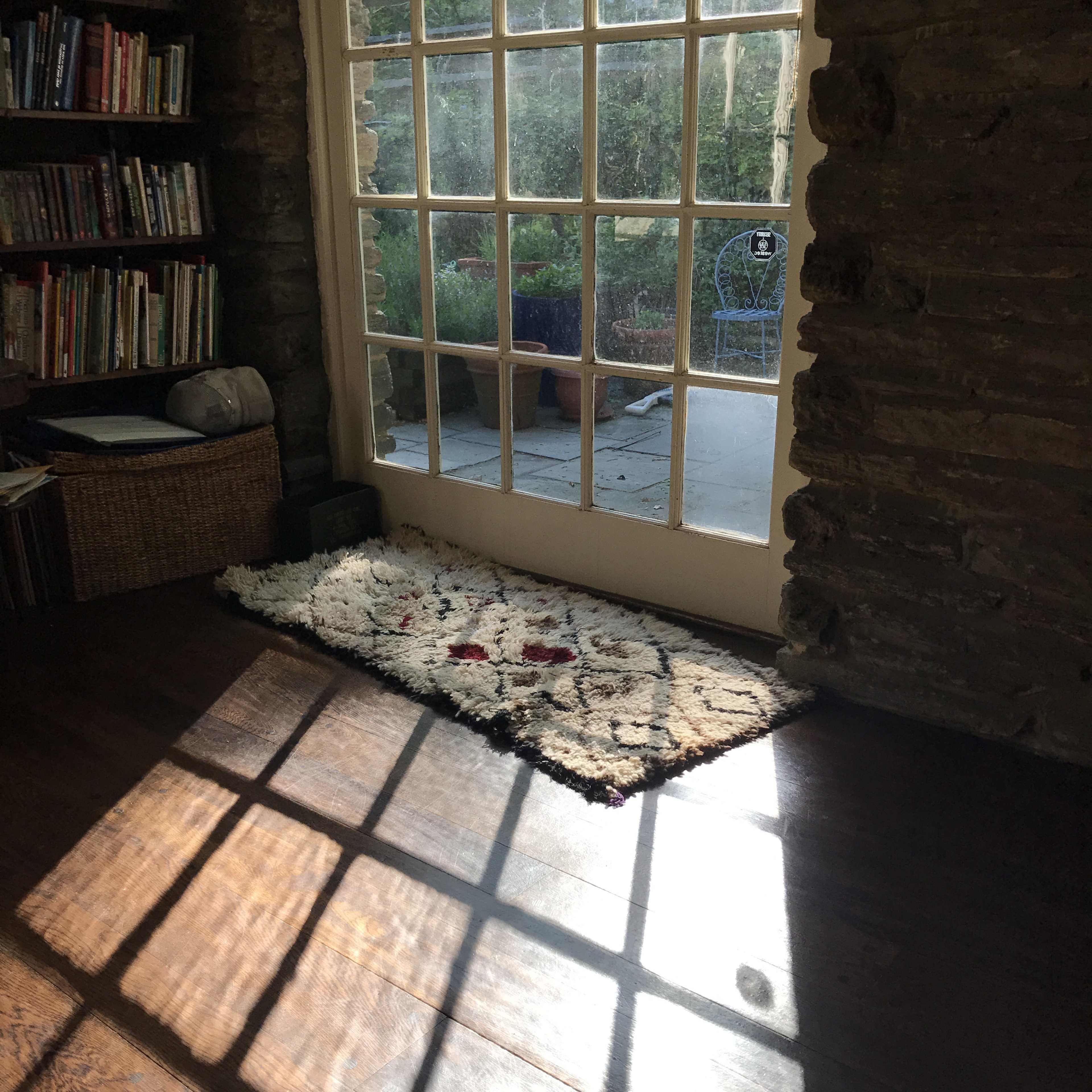 A cozy room with a woven rug positioned in front of a large window, allowing sunlight to create shadows on the wooden floor.