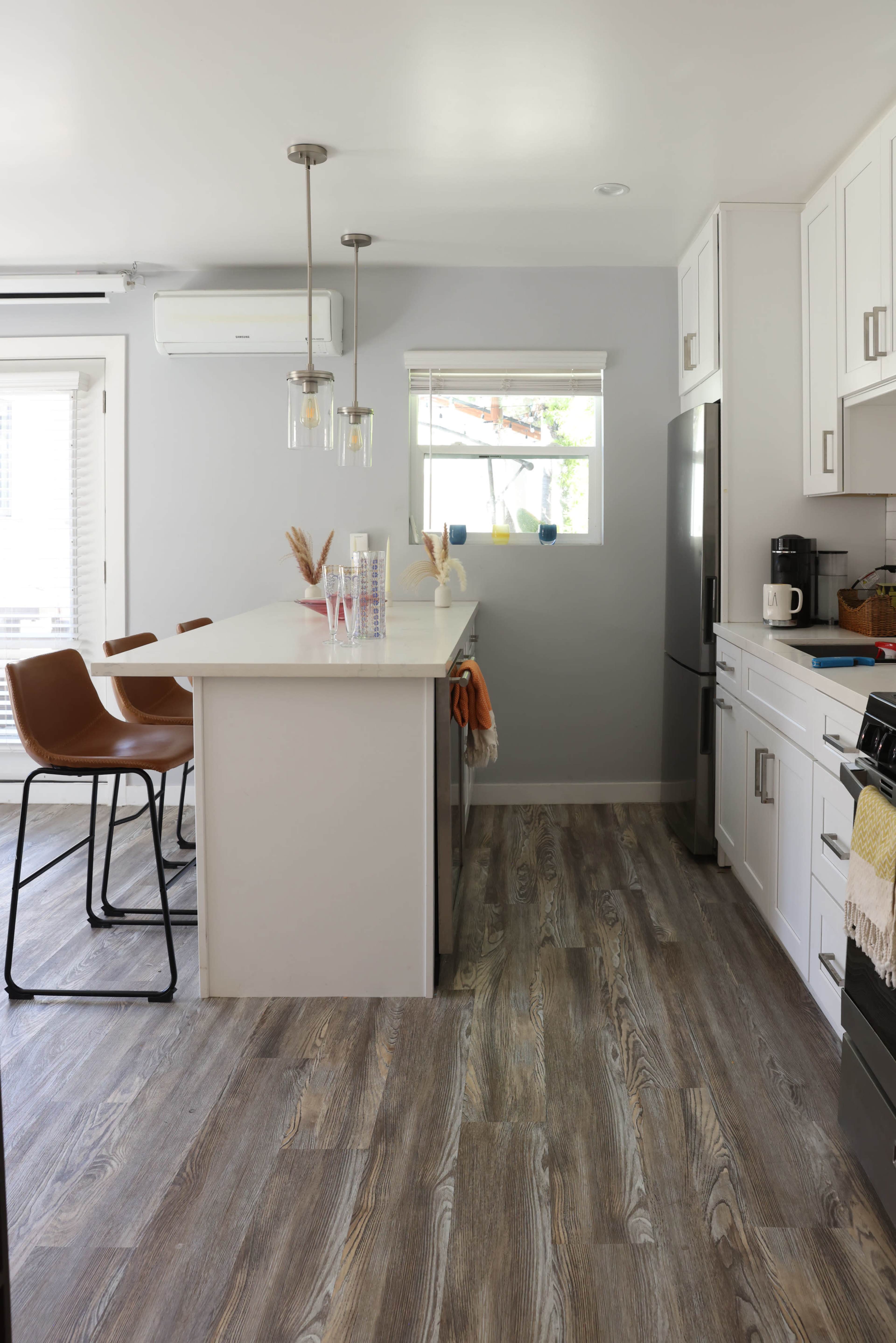 A modern kitchen features a light gray color scheme, an island with bar stools, and stainless steel appliances.