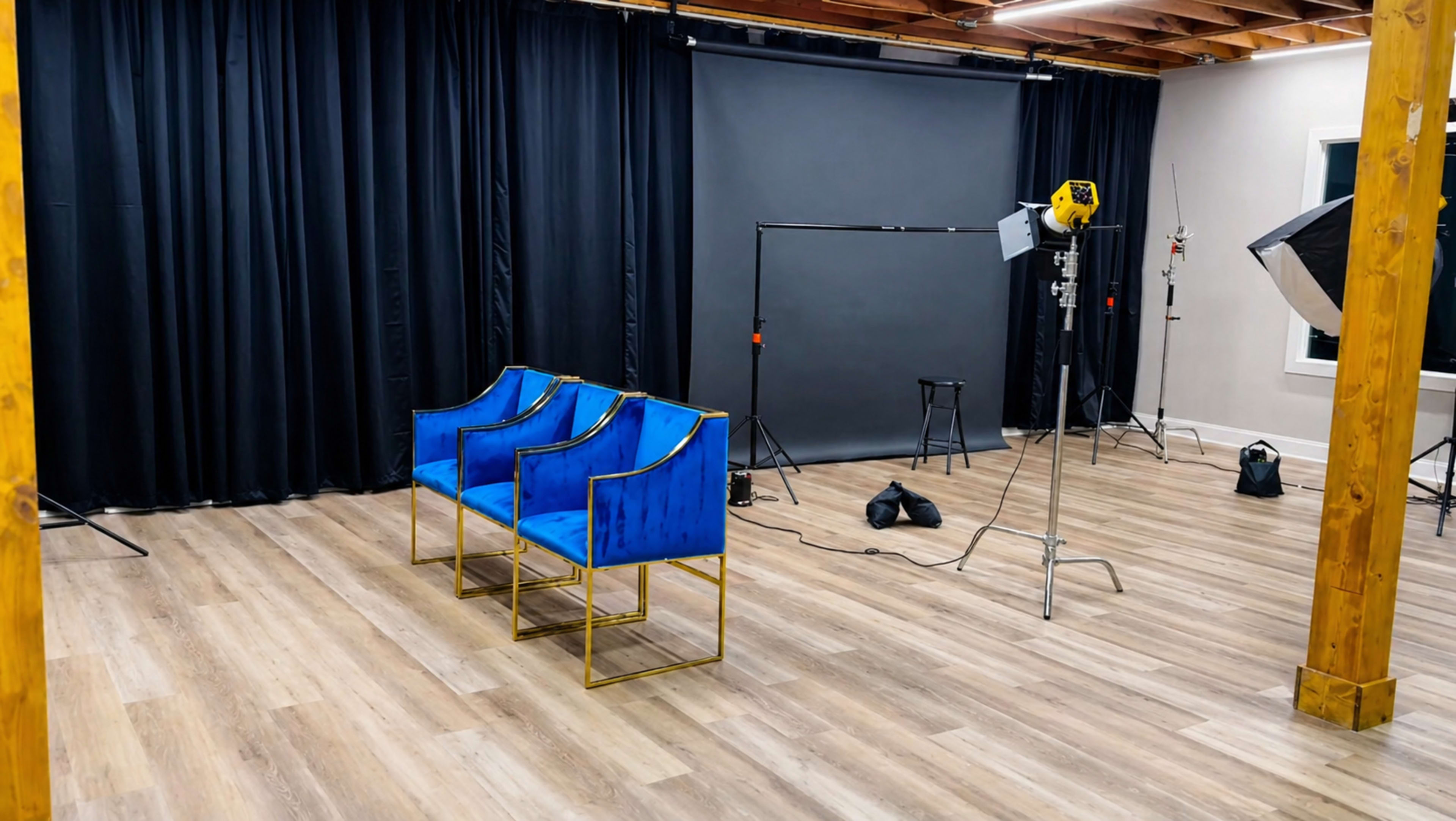 The image shows a photography studio featuring three blue chairs, a backdrop, and various lighting equipment set up in the space.
