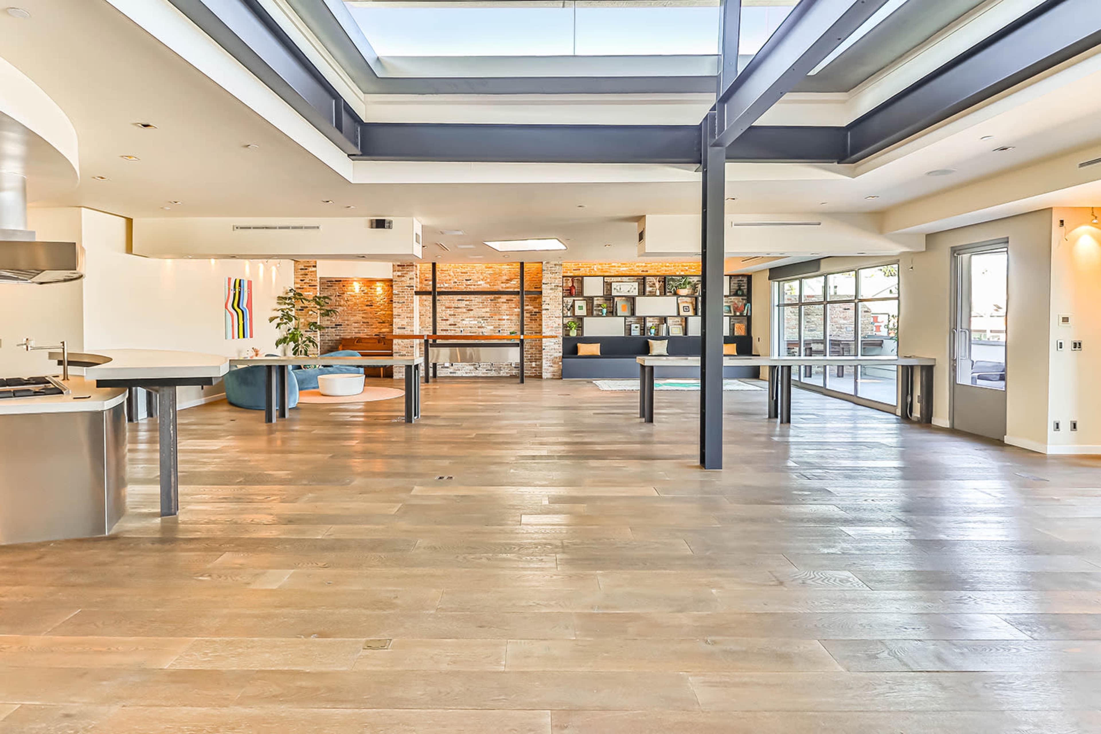A spacious, modern interior with wooden floors, large windows, and an open layout that includes a kitchen, living area, and seating space.
