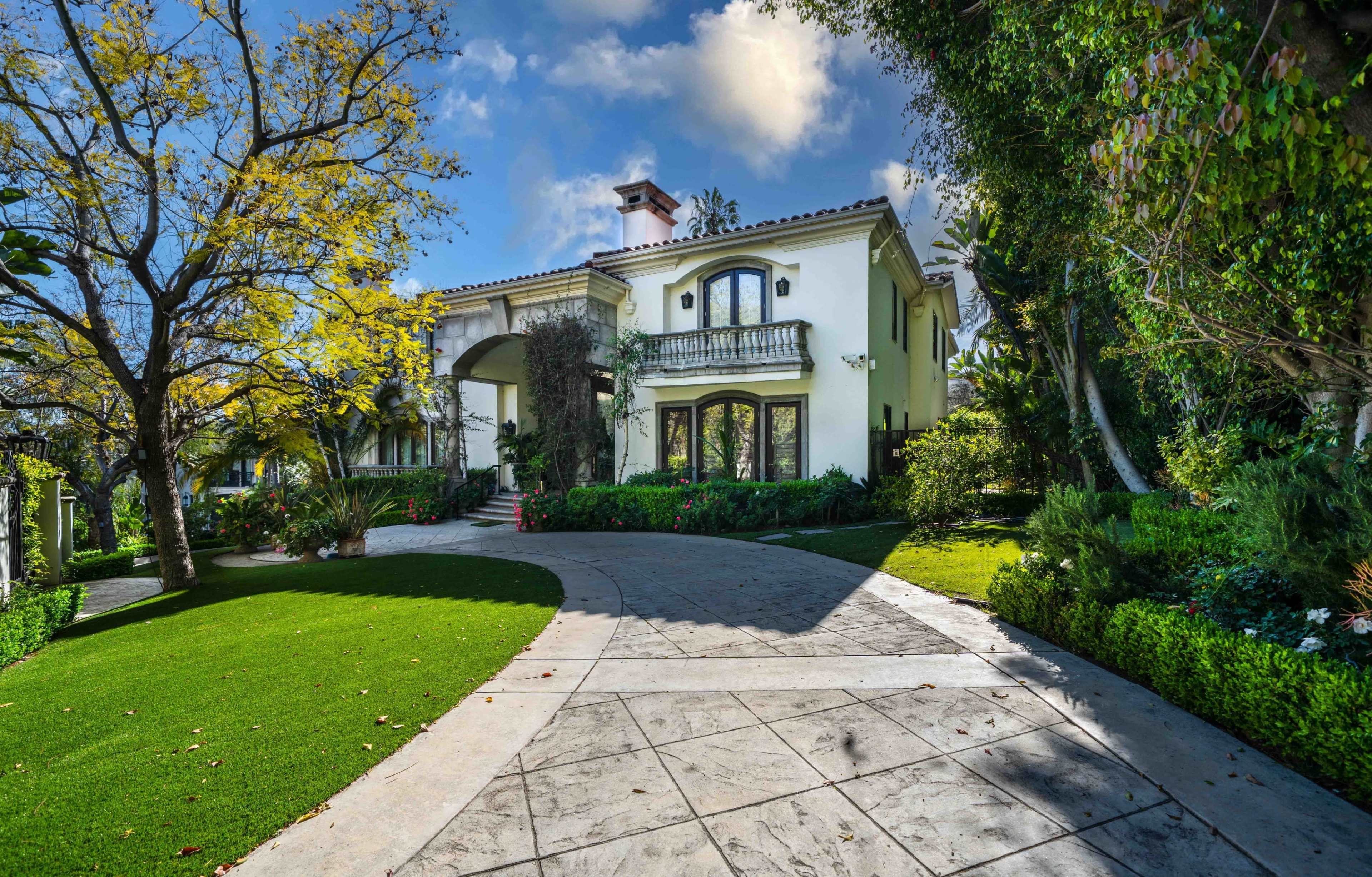A large, elegant house with a curved driveway is framed by well-manicured lawns and trees.