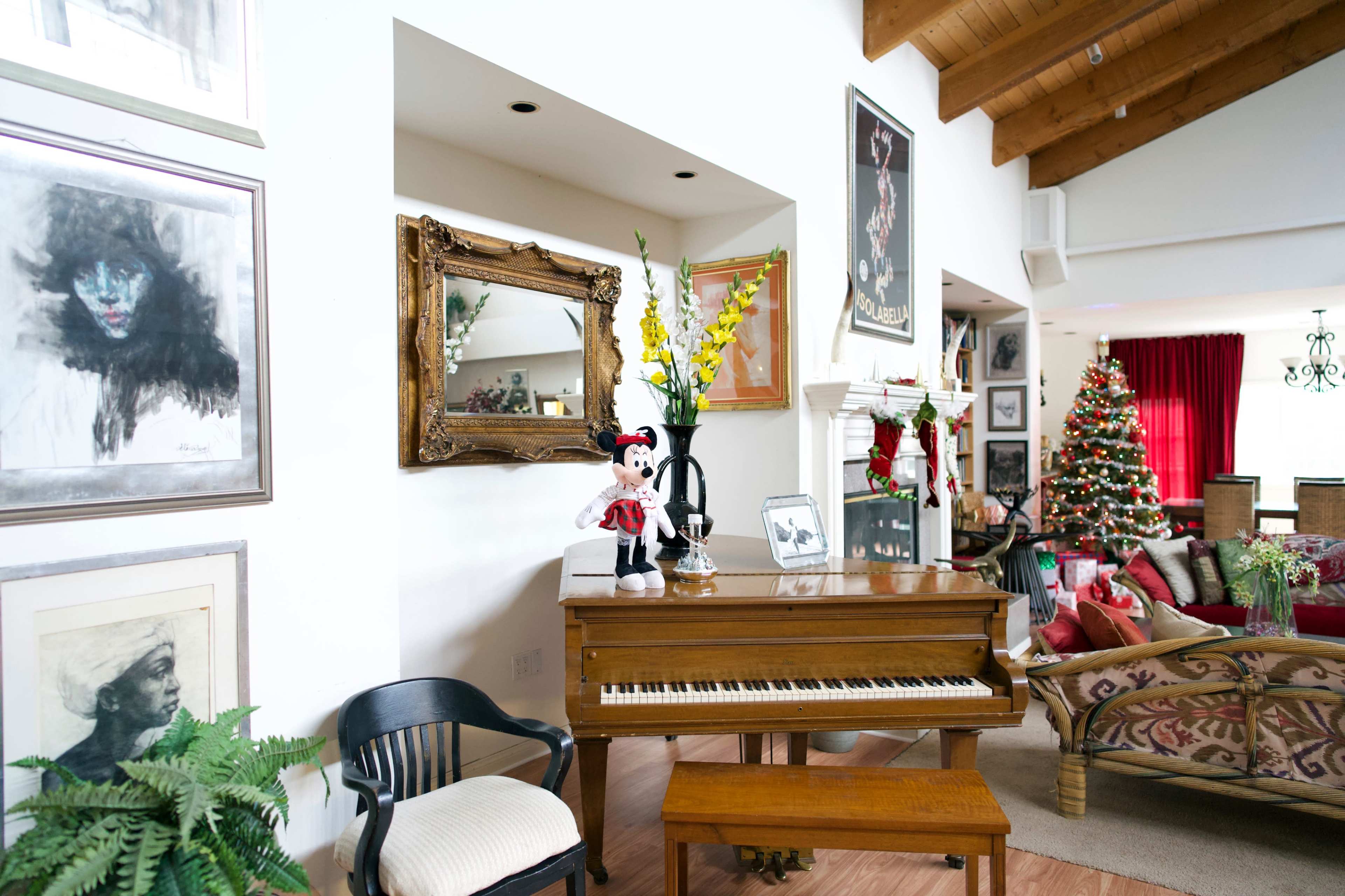 A living room featuring a piano, a Christmas tree, framed artwork on the walls, and decorative plants.