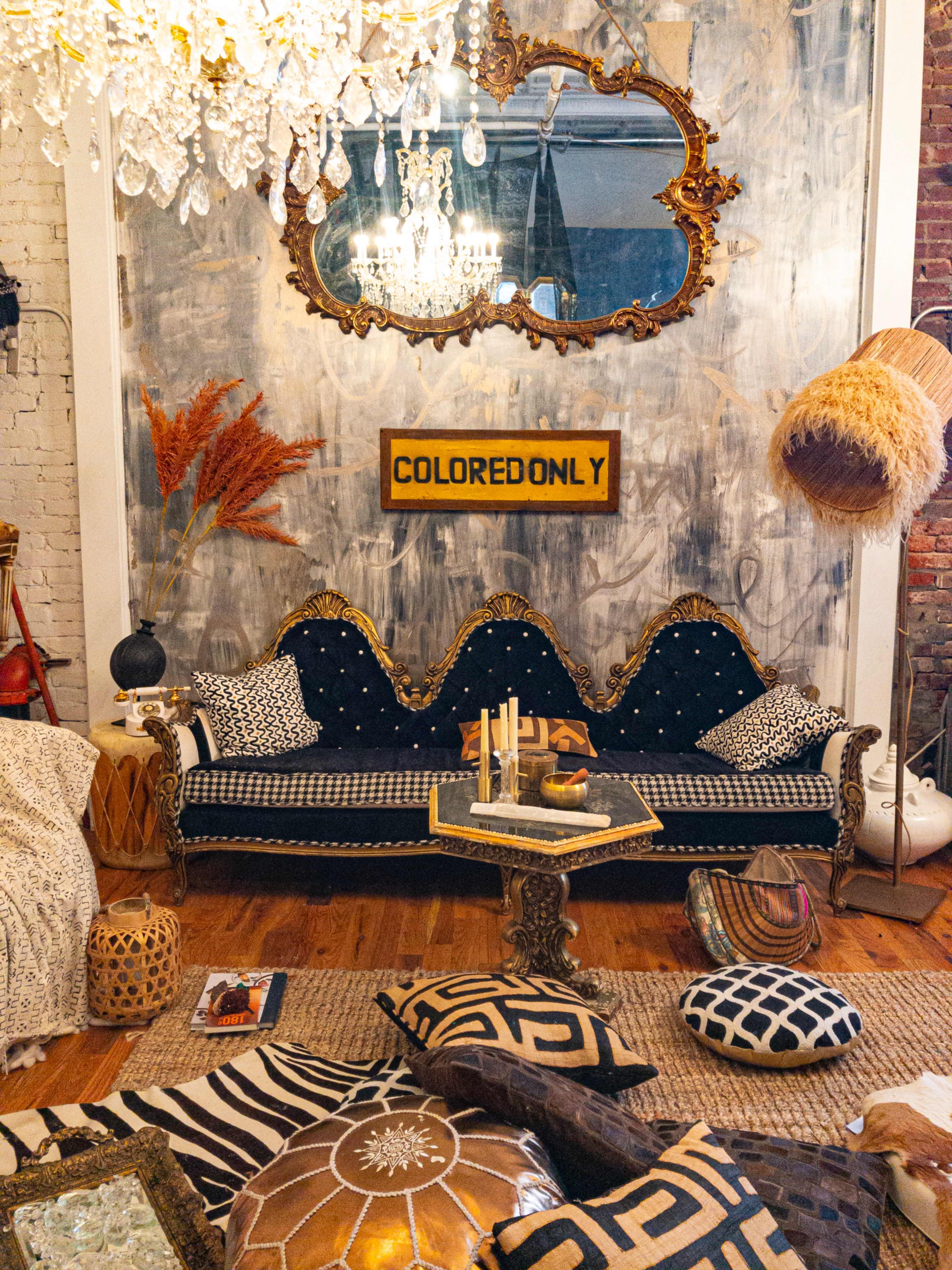 A vintage seating area features a patterned sofa with pillows, surrounded by decorative items and a large mirror against a textured wall.