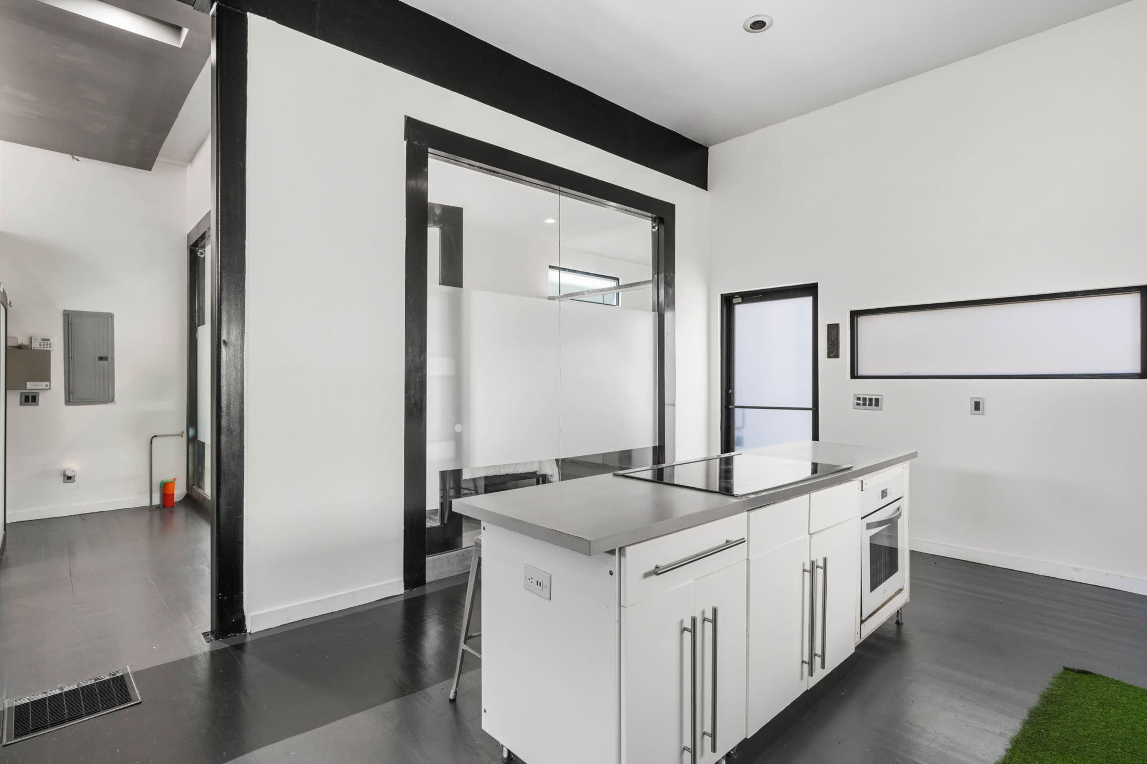 The image shows a modern kitchen with a central island and sleek cabinetry, adjacent to a glass-walled room.