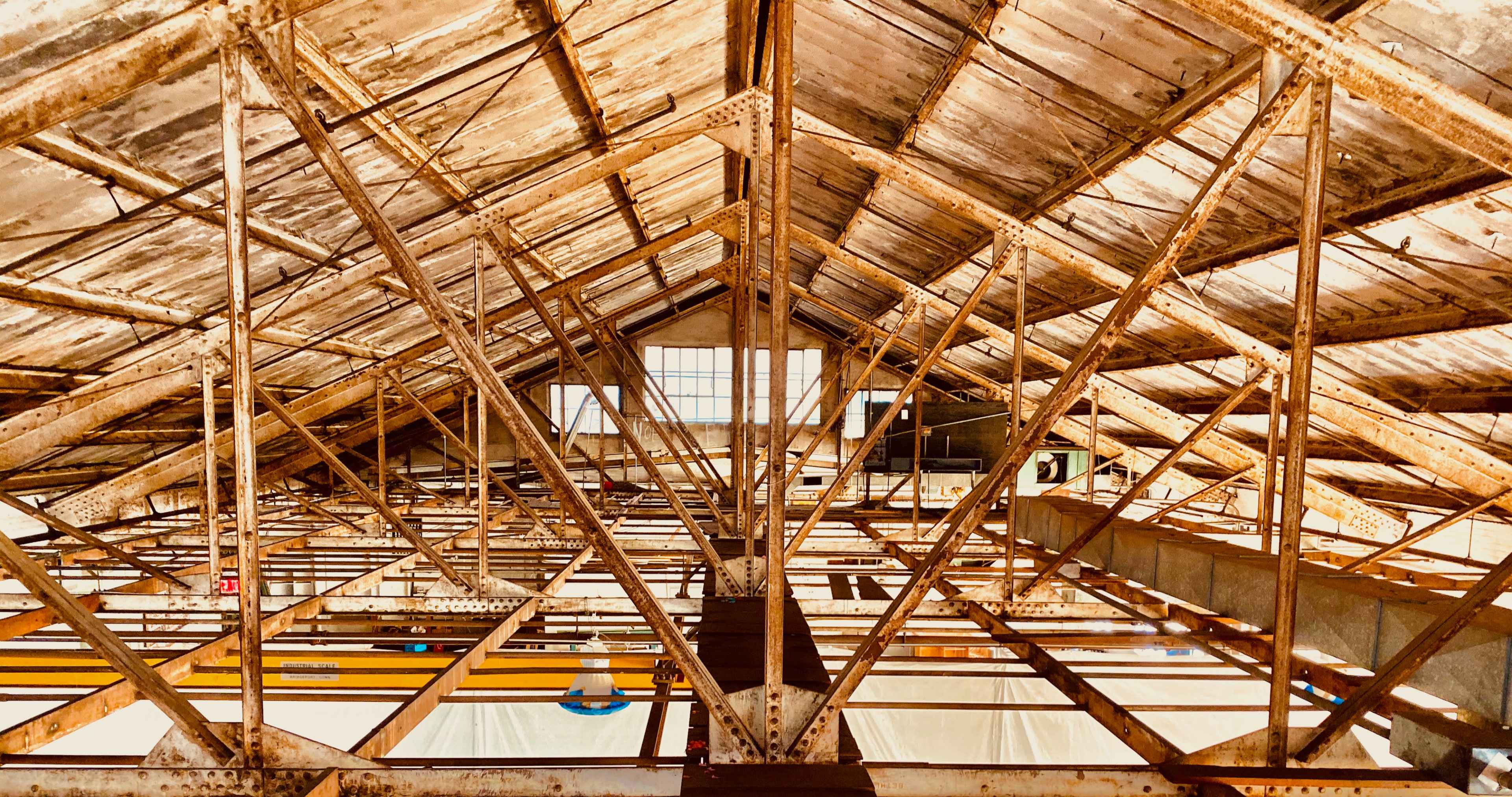 An industrial building's ceiling featuring exposed wooden beams and metal trusses with natural light illuminating the space.