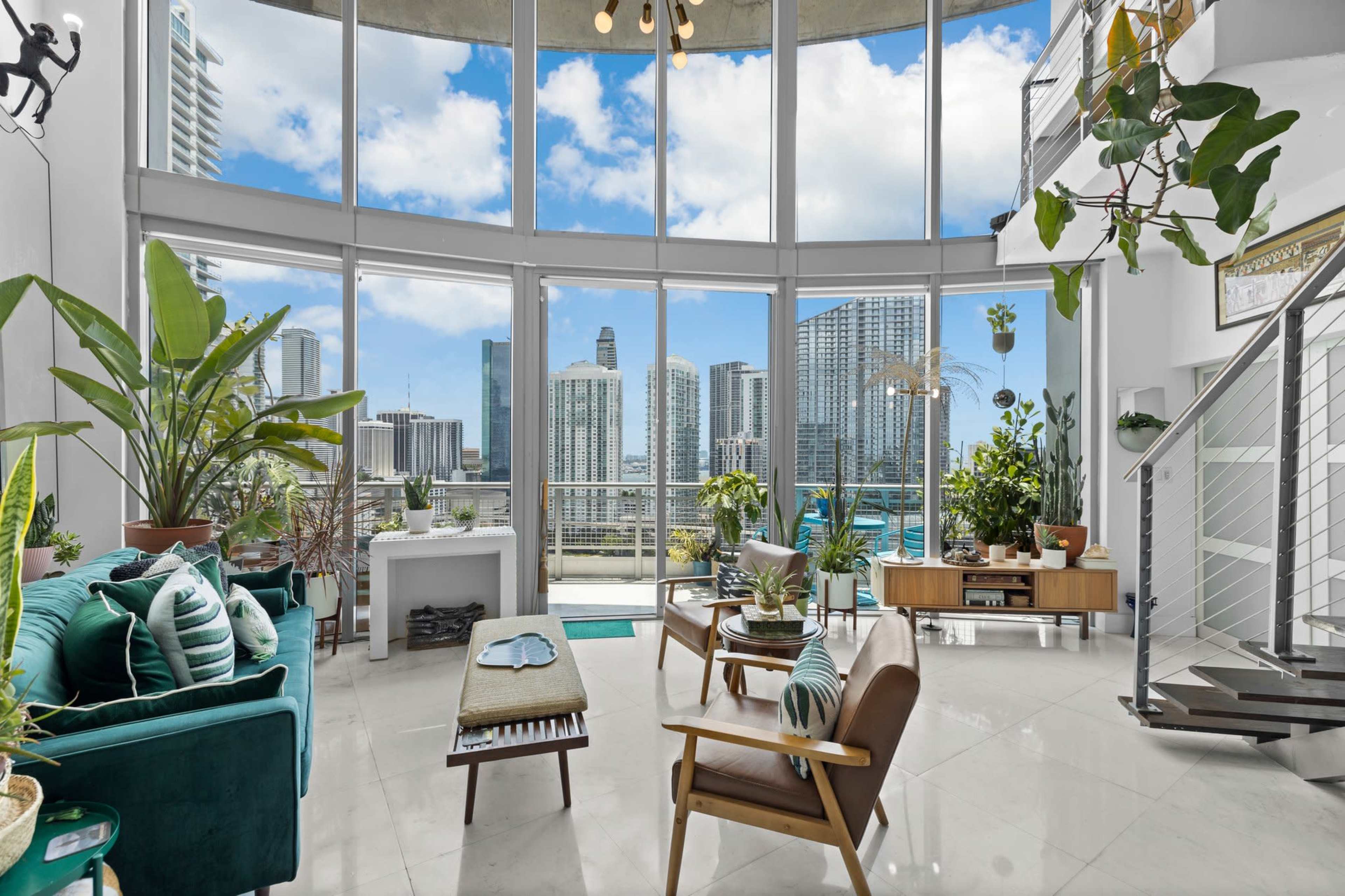 A modern, open living space with large windows overlooking a city skyline, filled with plants and stylish furniture.
