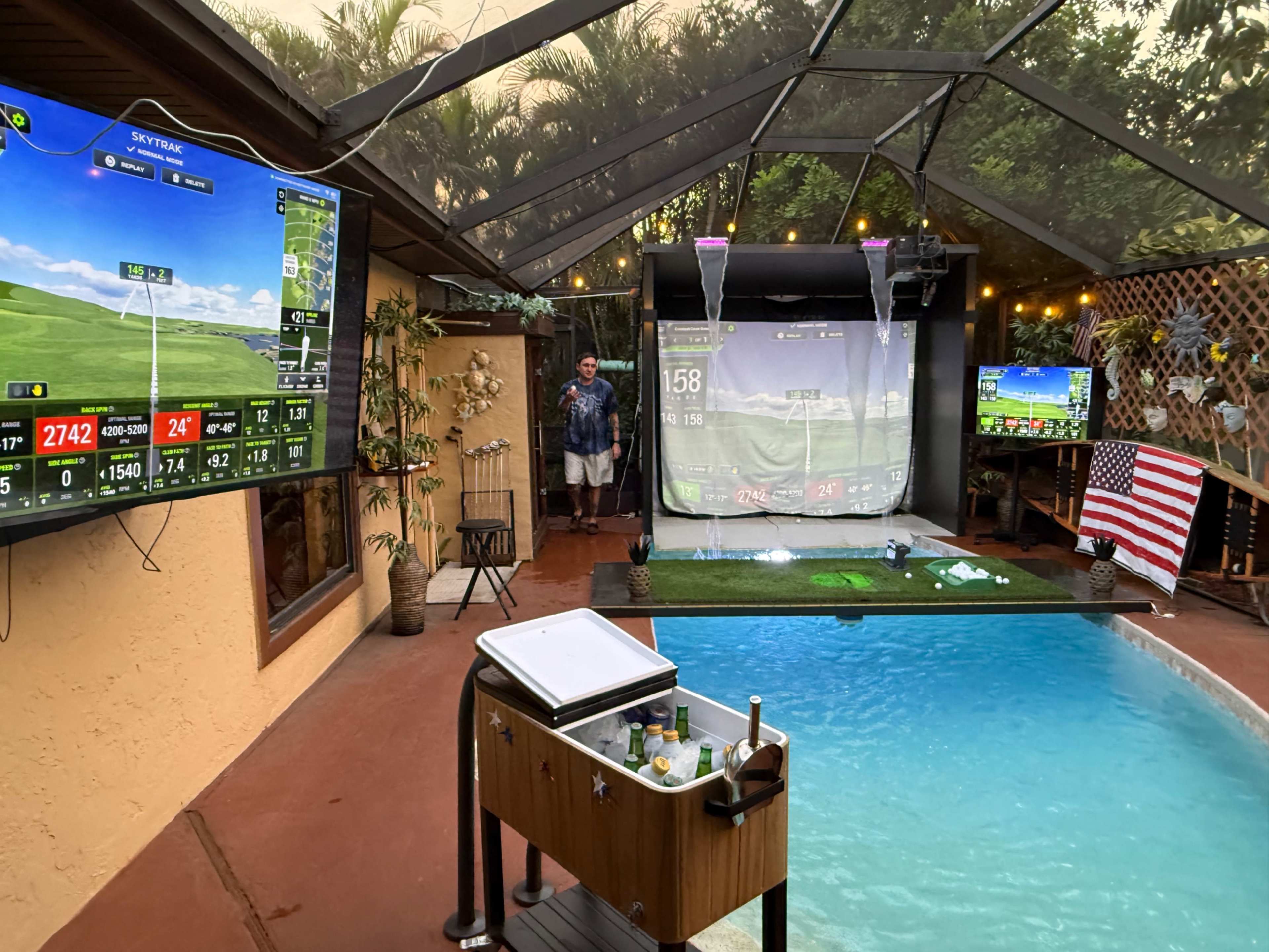 The scene features an indoor area with a pool, golf simulators on two screens, and a person standing near the entrance under a canopy.