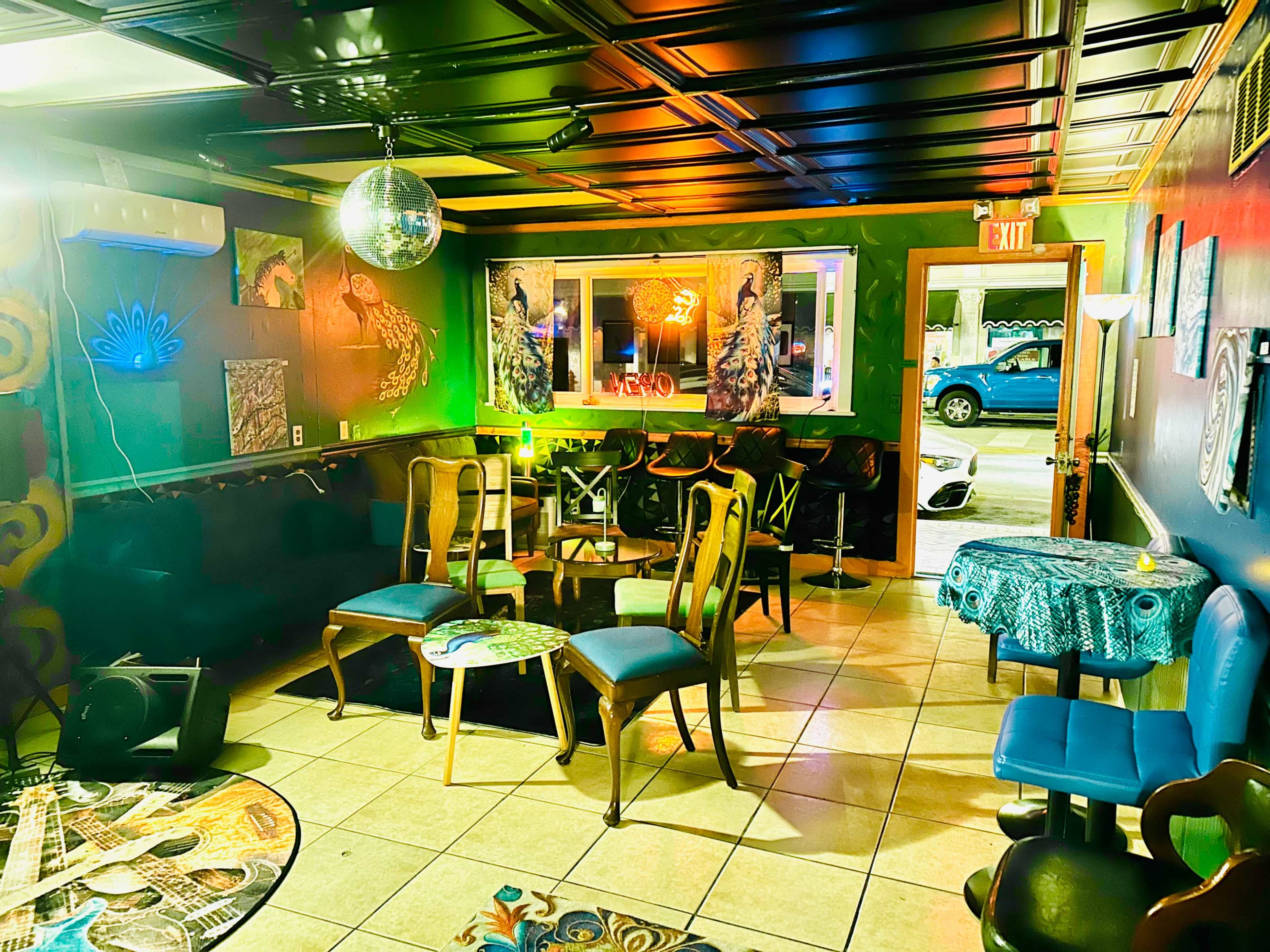 The image shows a colorful lounge area with chairs, tables, and a disco ball, featuring vibrant wall decor and lighting.