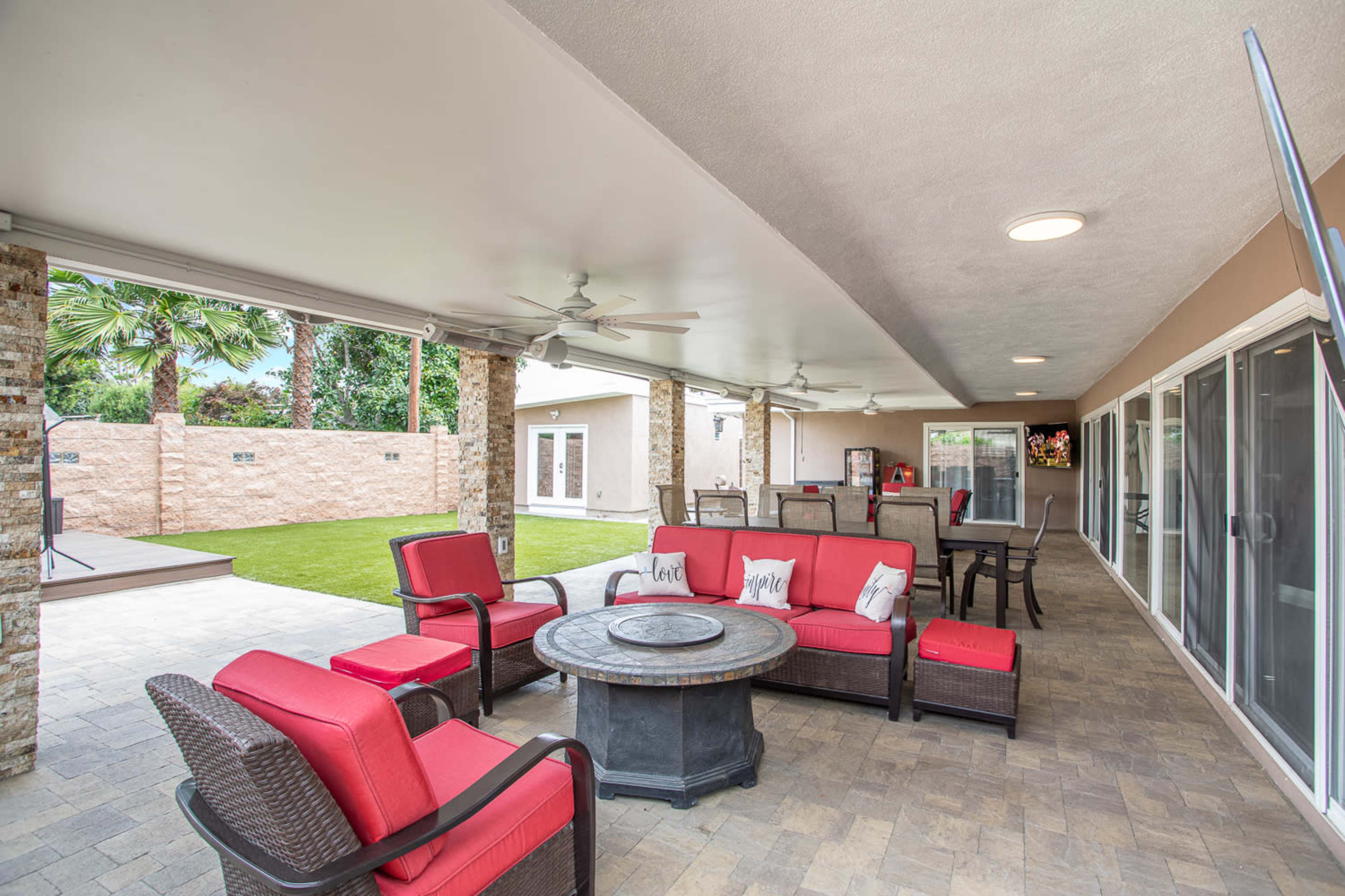 A spacious outdoor patio area with red cushioned seating, a round table at the center, and a grassy lawn in the background.