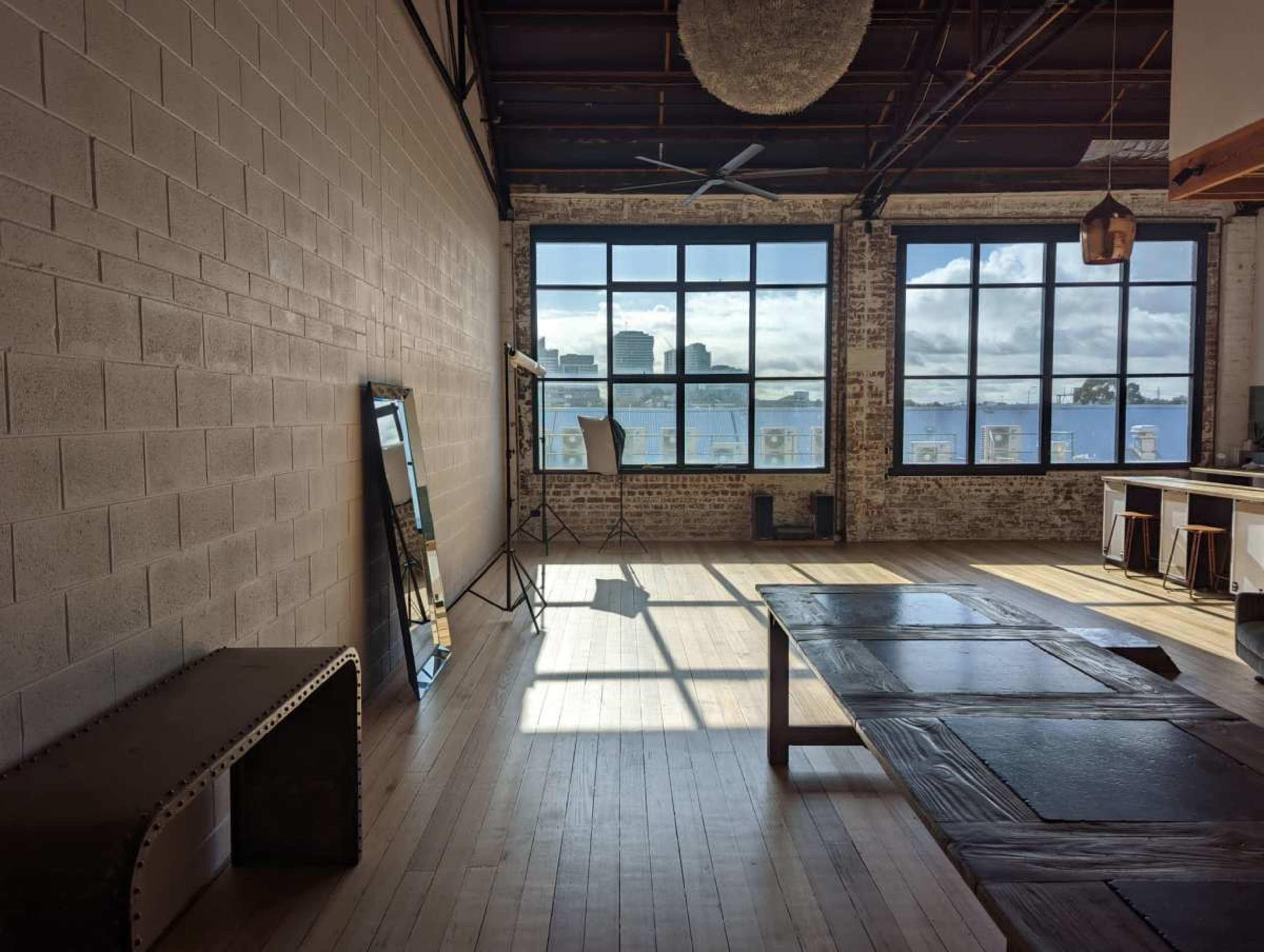 A spacious, well-lit room with large windows offers a view of a city skyline and features wooden floors and minimalist furniture.