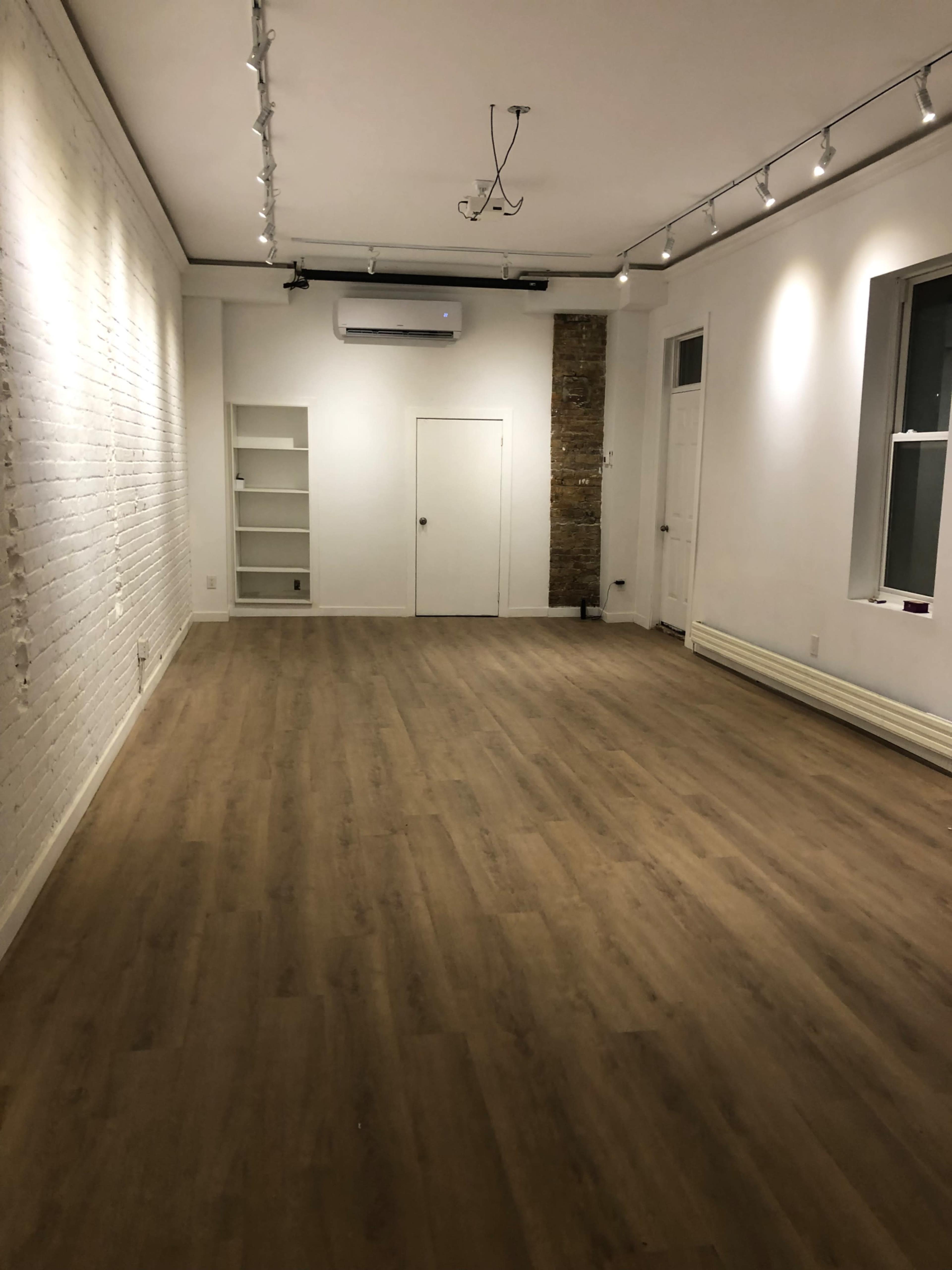 An empty room with wooden flooring, white brick walls, and a single built-in bookshelf on one side.