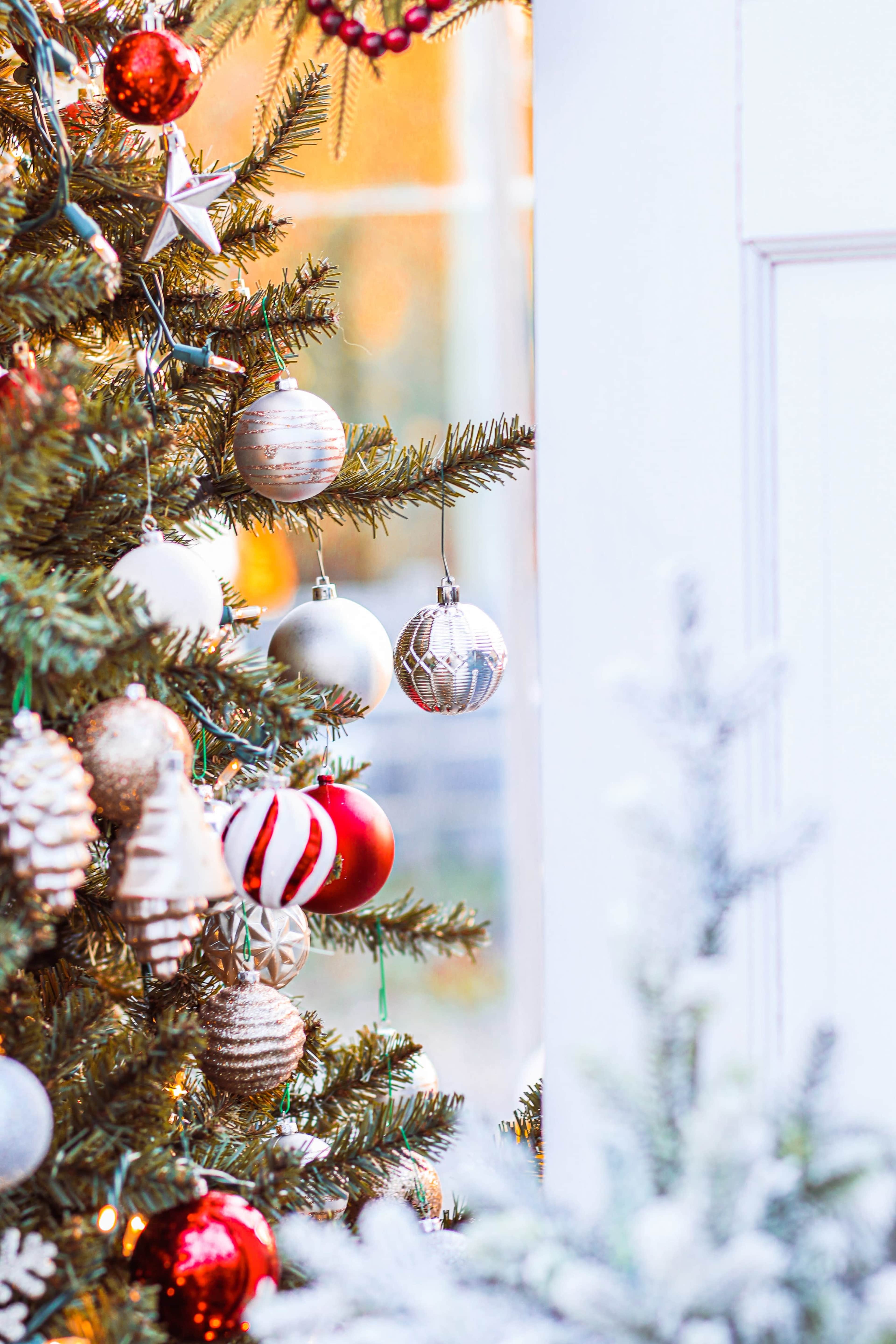 A decorated Christmas tree is positioned near a window, adorned with various colorful ornaments and pinecones.
