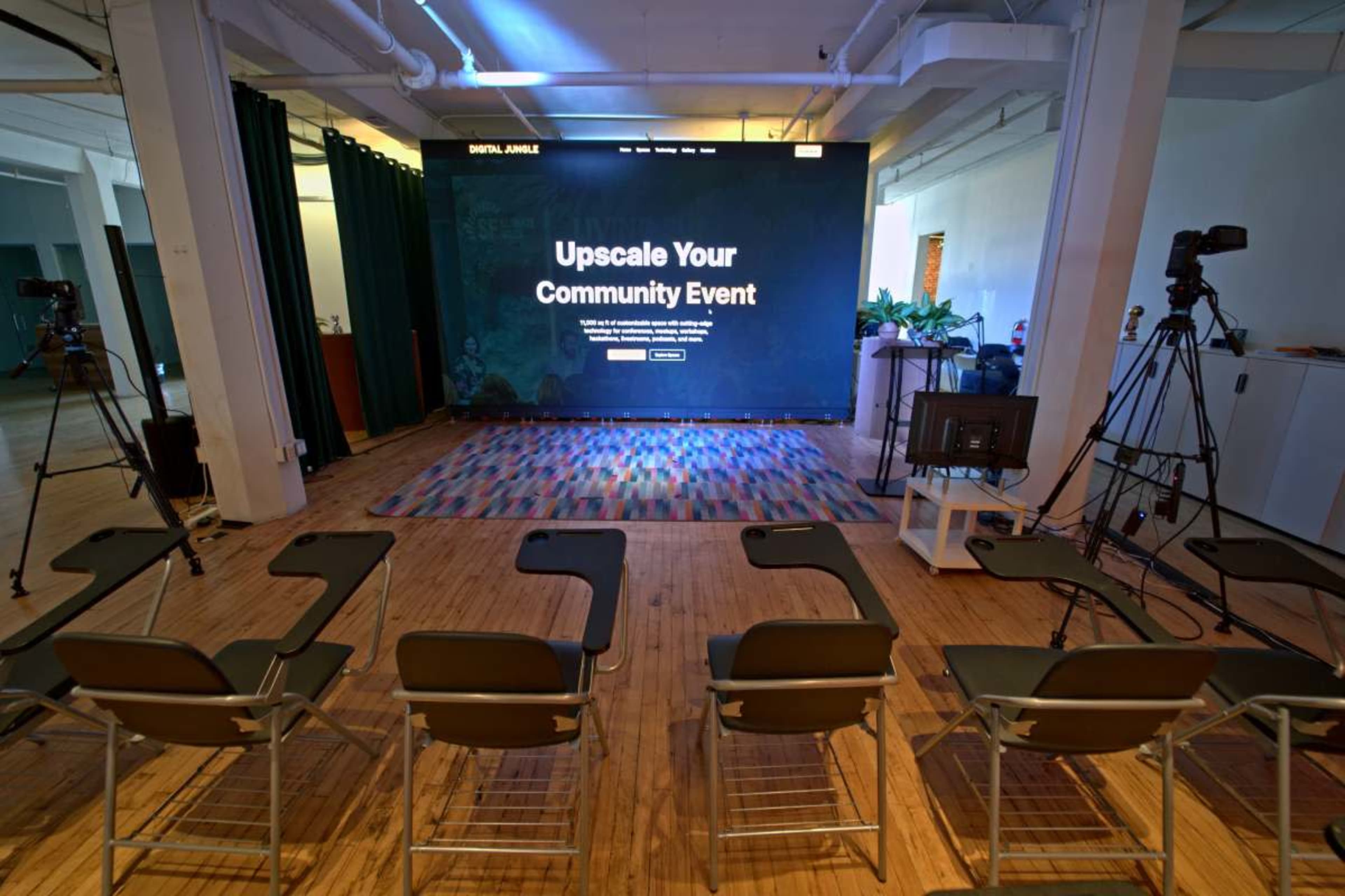 The image shows a room set up for a presentation, featuring a large screen displaying "Upscale Your Community Event," with several empty chairs arranged in front of it.