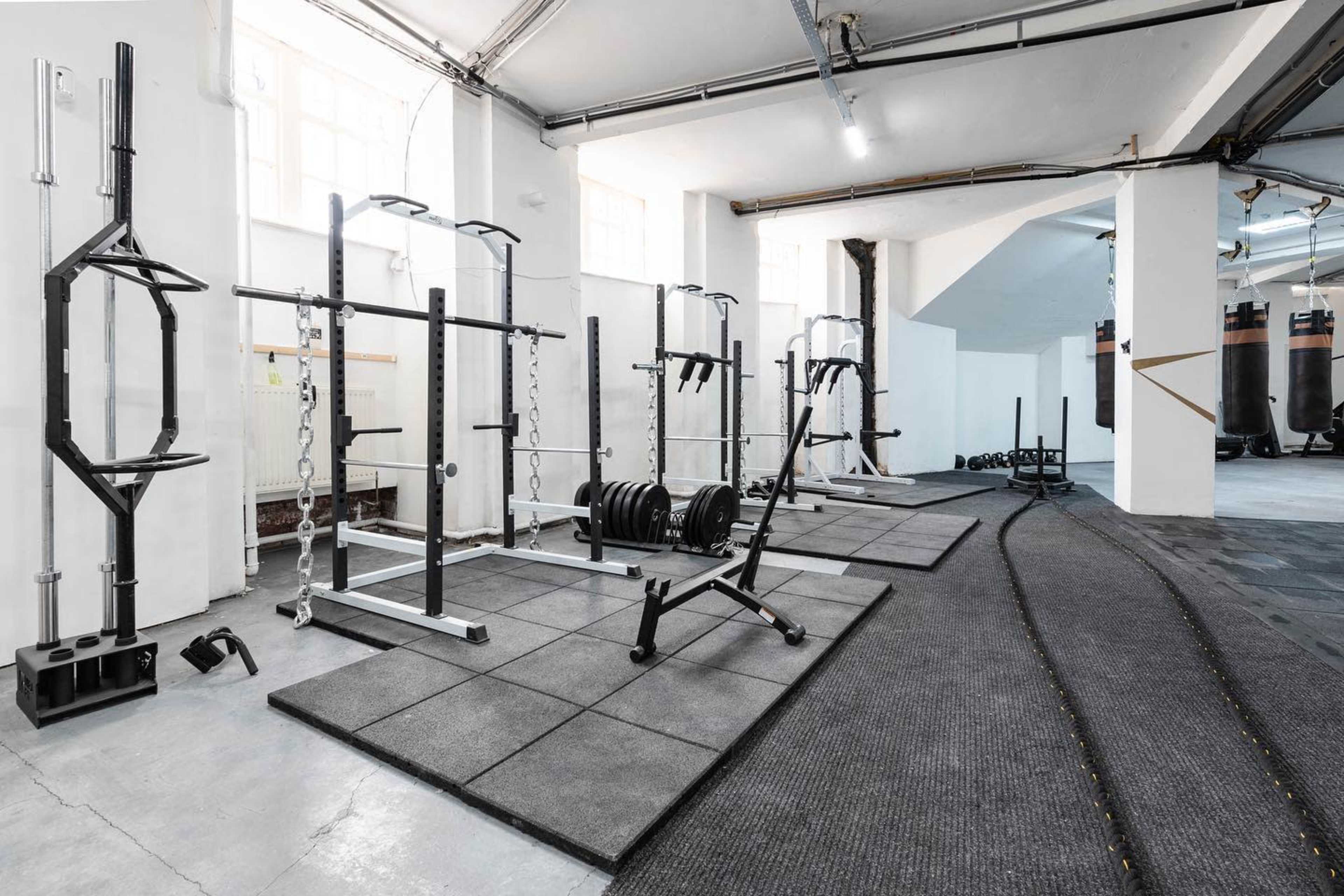 A well-equipped gym featuring weightlifting racks, free weights, and exercise mats arranged in a spacious room with ample natural light.