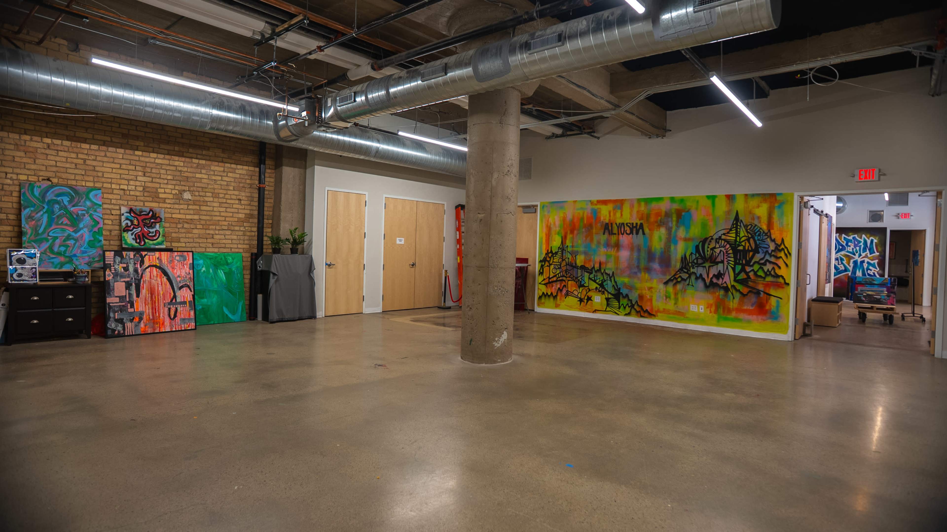 The image shows an open indoor space with polished concrete floors, exposed ductwork, and colorful graffiti art on the walls.