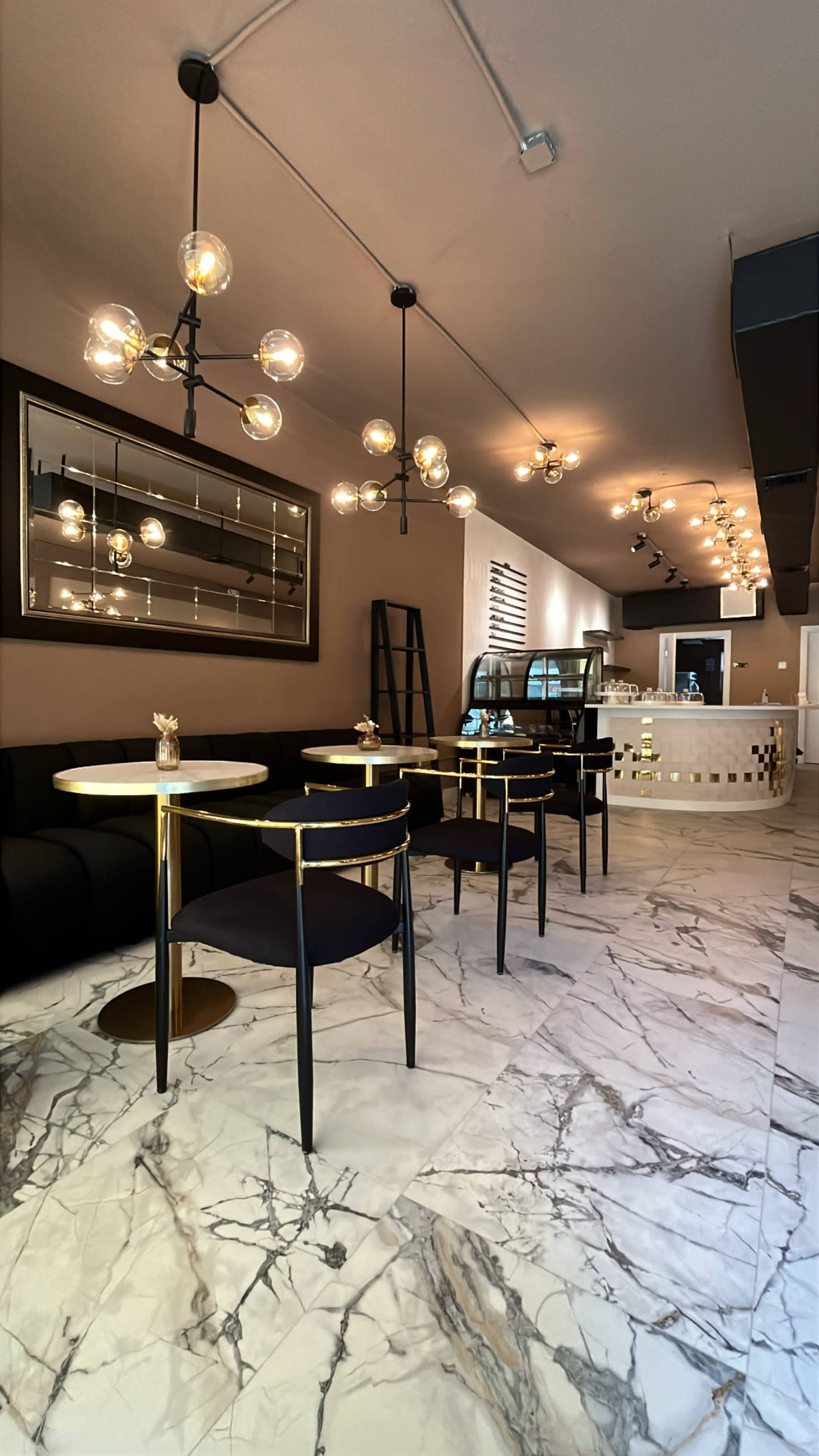 The image shows a modern café interior with marble flooring, circular tables, black chairs, and pendant lighting.