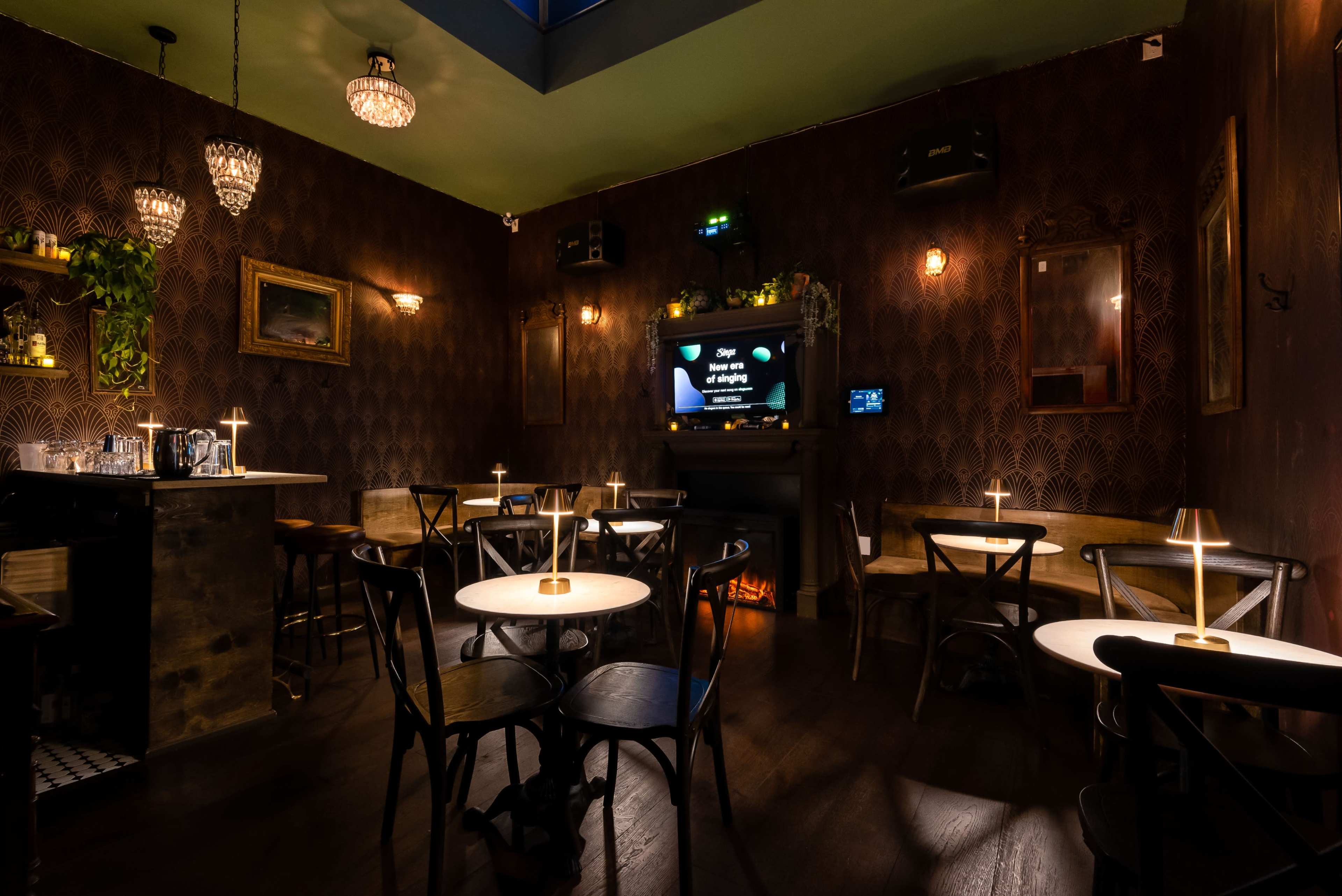 The image shows a dimly lit café with dark wallpaper, small round tables, and a bar area, creating an intimate atmosphere.