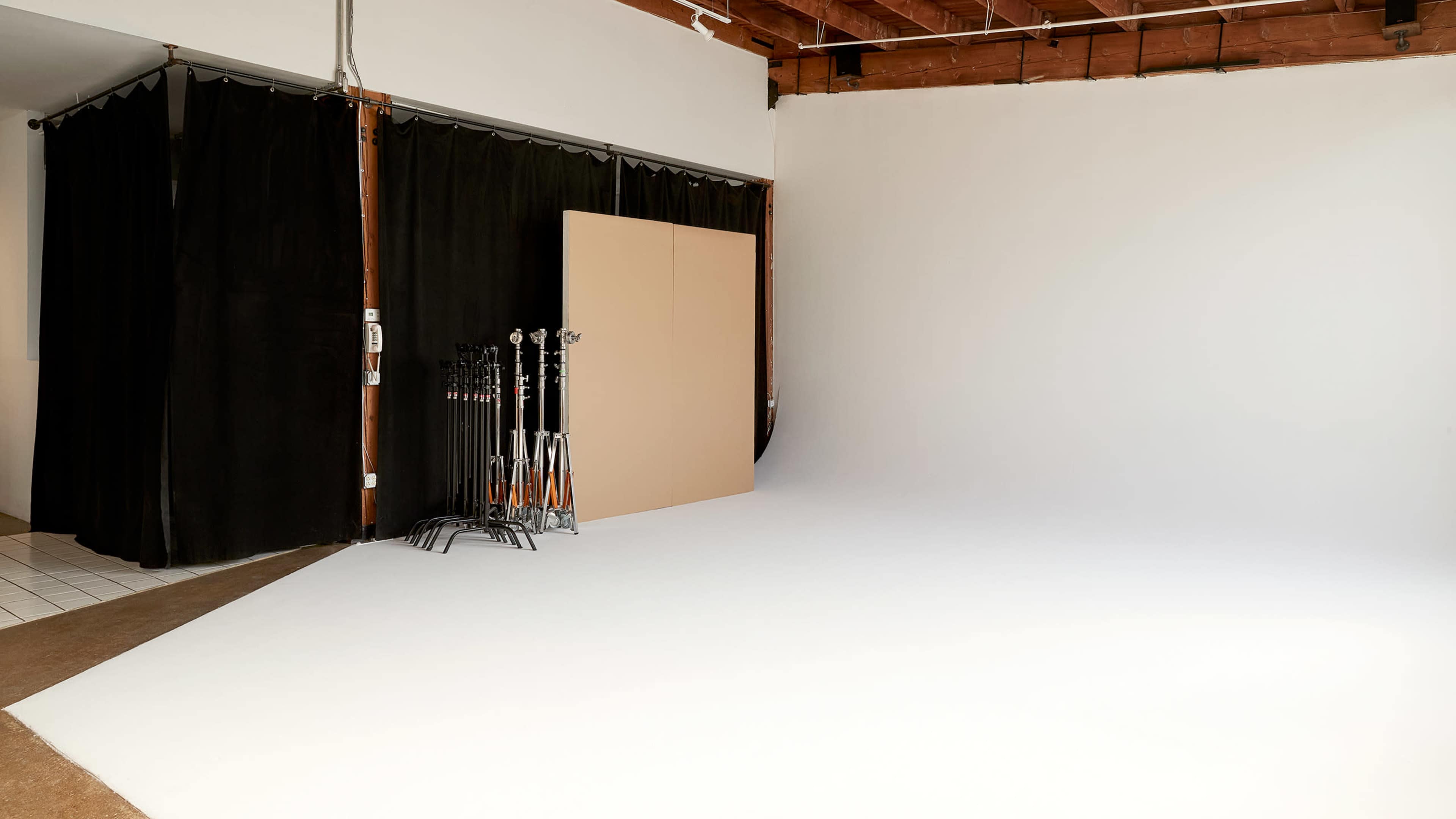 The image shows a photography studio featuring a white backdrop, black curtains, and several light stands on a support rack.
